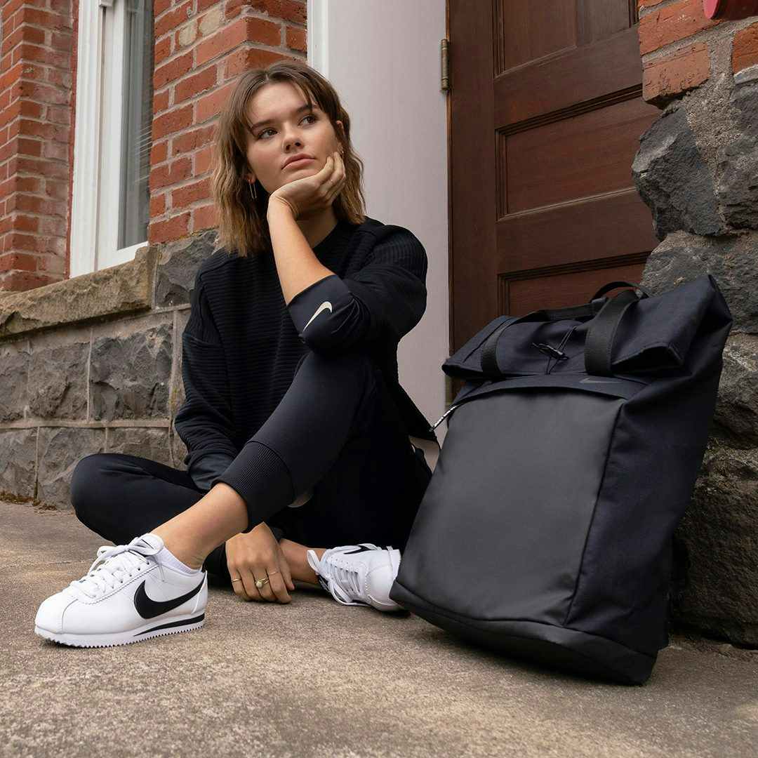 girl in cheap nike gear sits by a wall with her chin resting on her hand