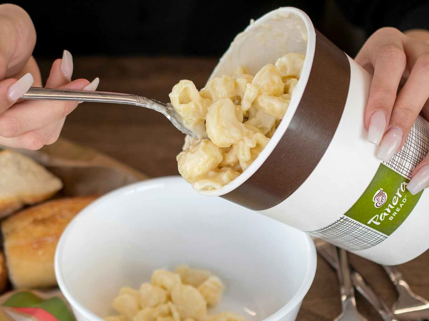 person spooning out macaroni and cheese from panera family box container