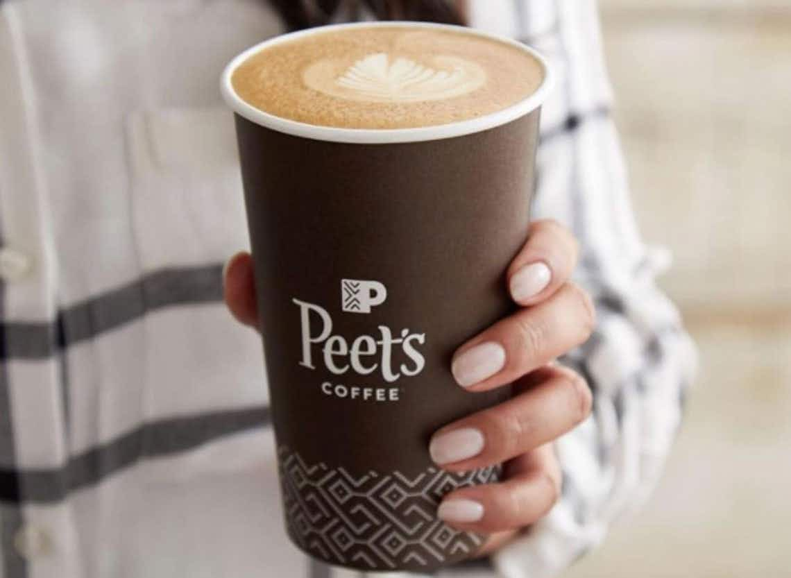 A person holding a cup that says Peets filled with foamy coffee