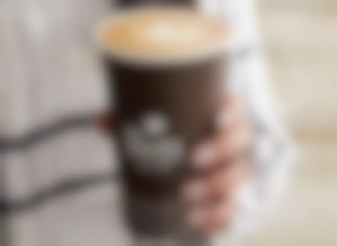 A person holding a cup that says Peets filled with foamy coffee