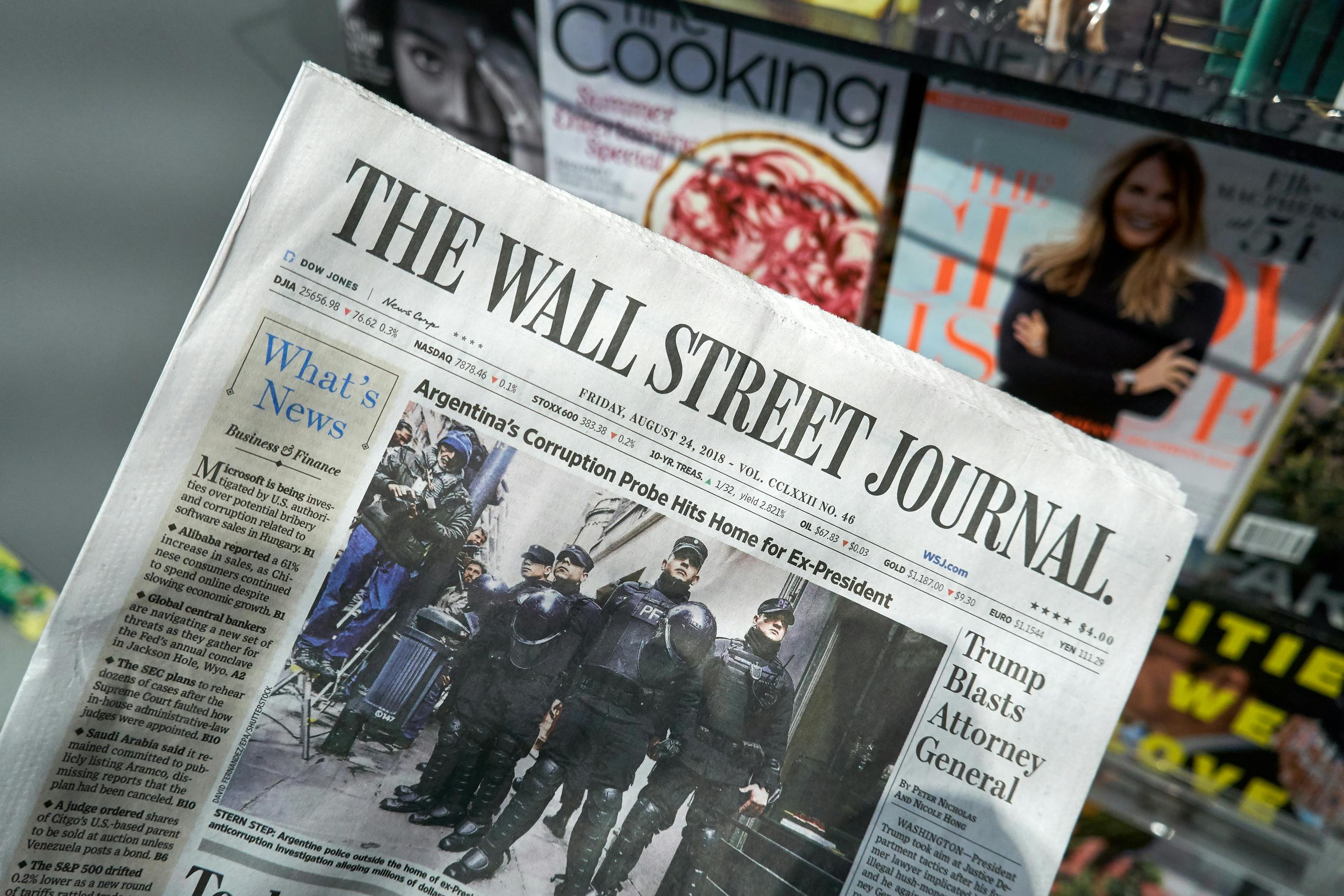 A copy of the Wall Street Journal held up in front of an outdoor newspaper stand.