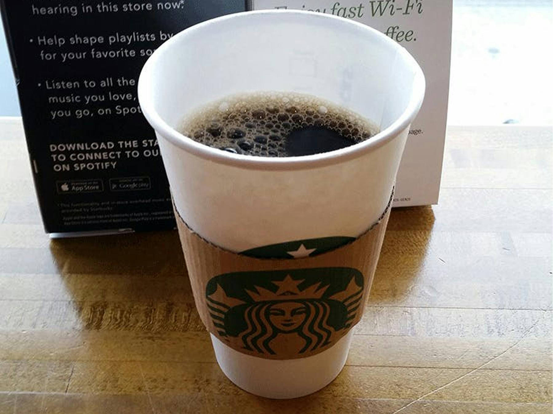 A Starbucks tall black coffee in a grande cup sitting on a table.