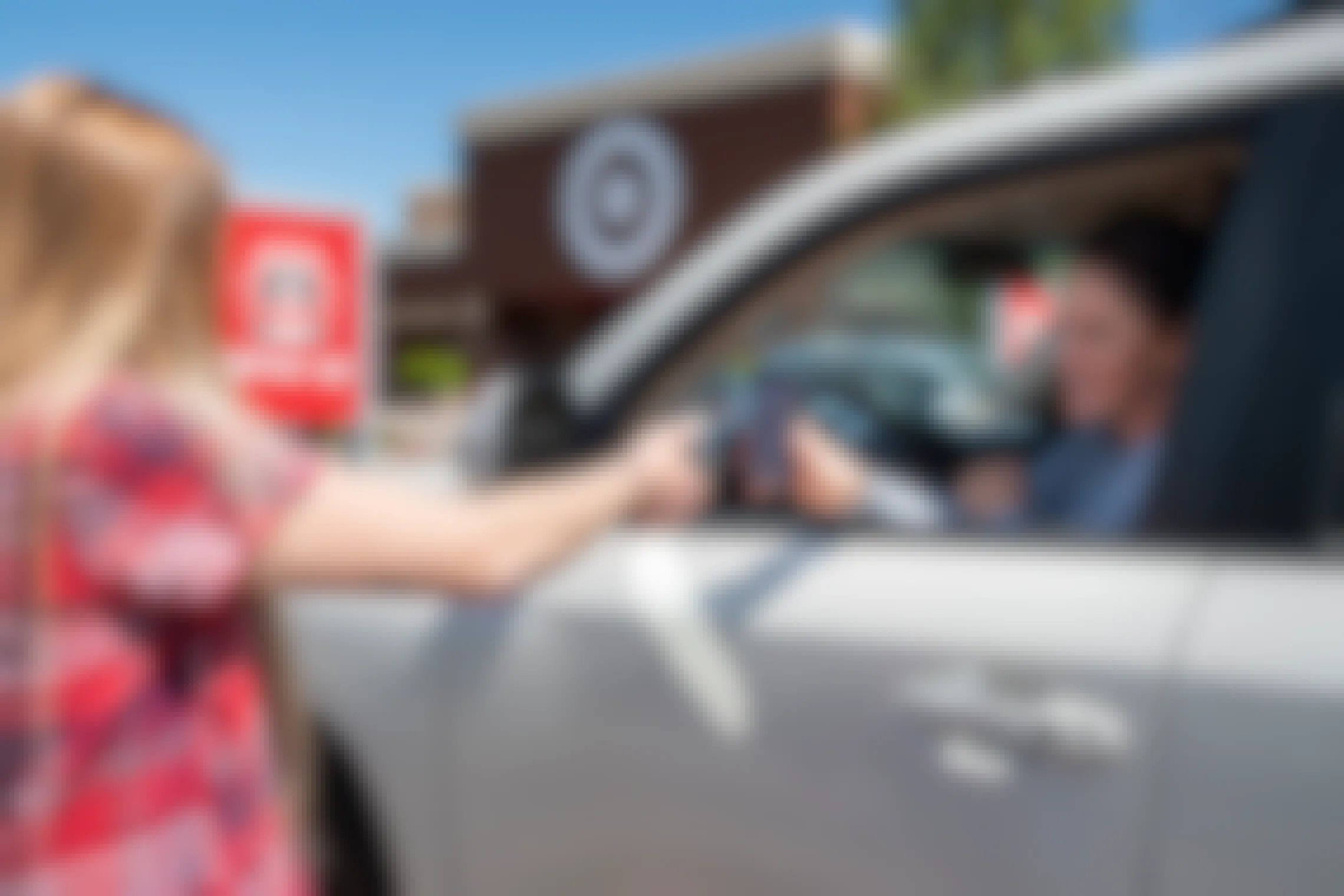 A woman sitting in her vehicle in the curbside Drive Up parking spot outside of Target, holding her phone out to be scanned by a Target employee.