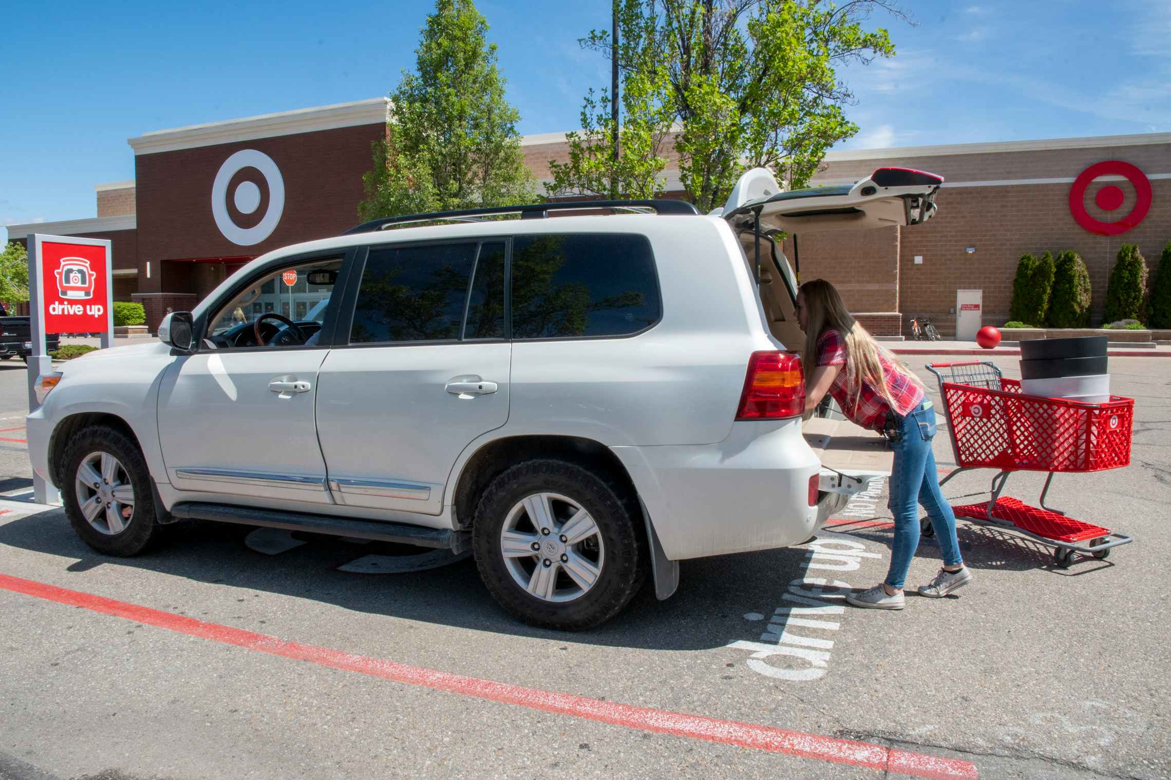 A person standing next to a Target cart, reaching into the open trunk of a vehicle parked in the Drive Up parking spot outside of Target.