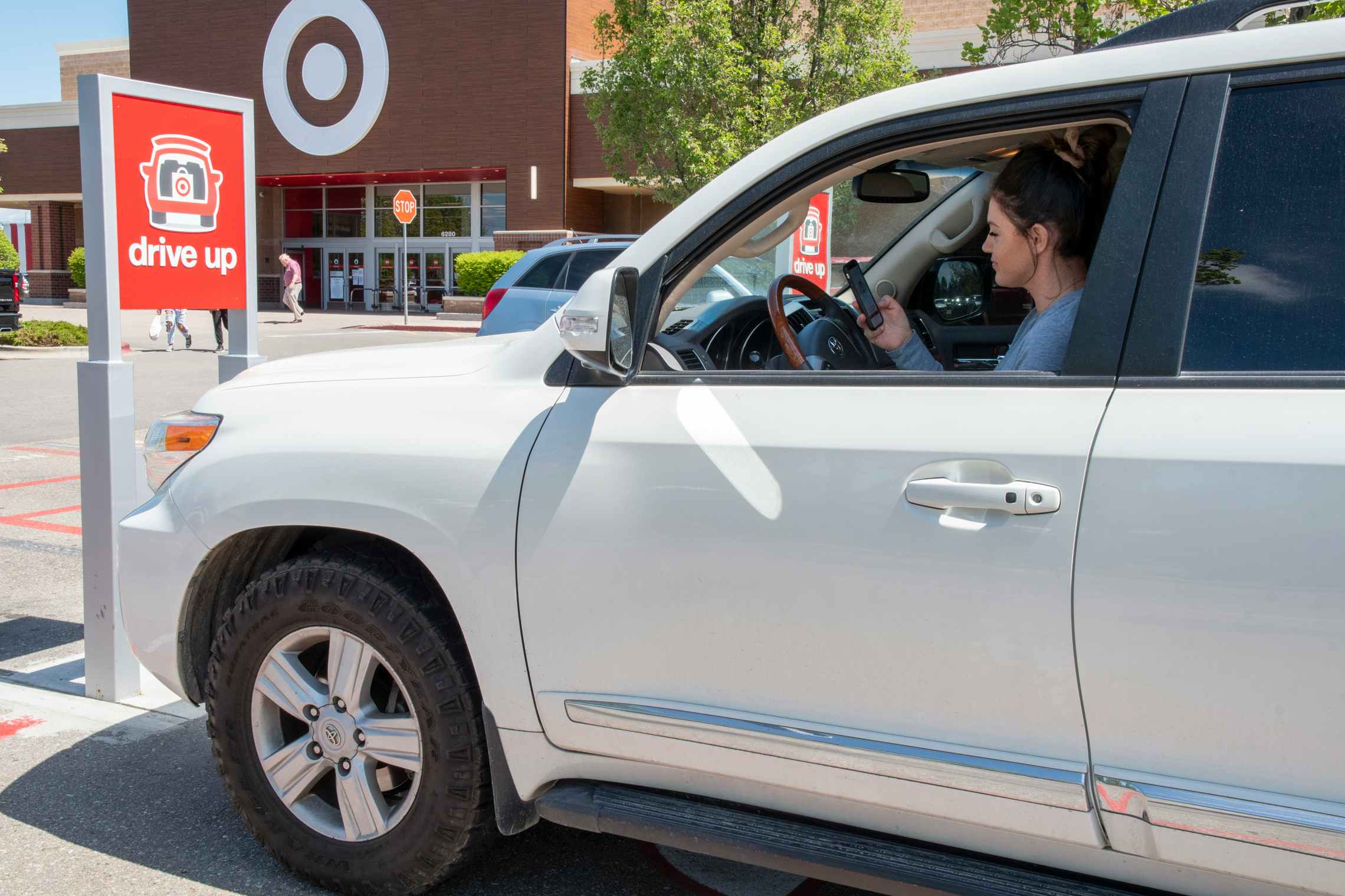 A person sitting in a car that is parked in the Target parking spot for Drive Up orders, looking down at a phone.