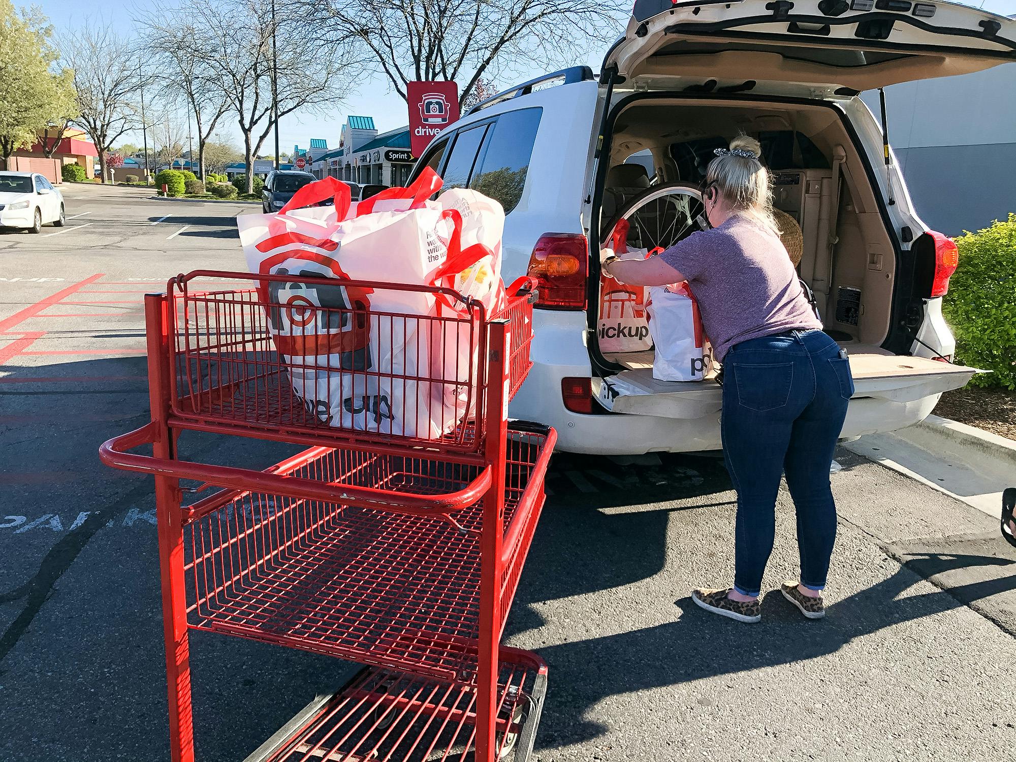 A person loading bags of groceries into the trunk of a vehicle next to a Target shopping cart.