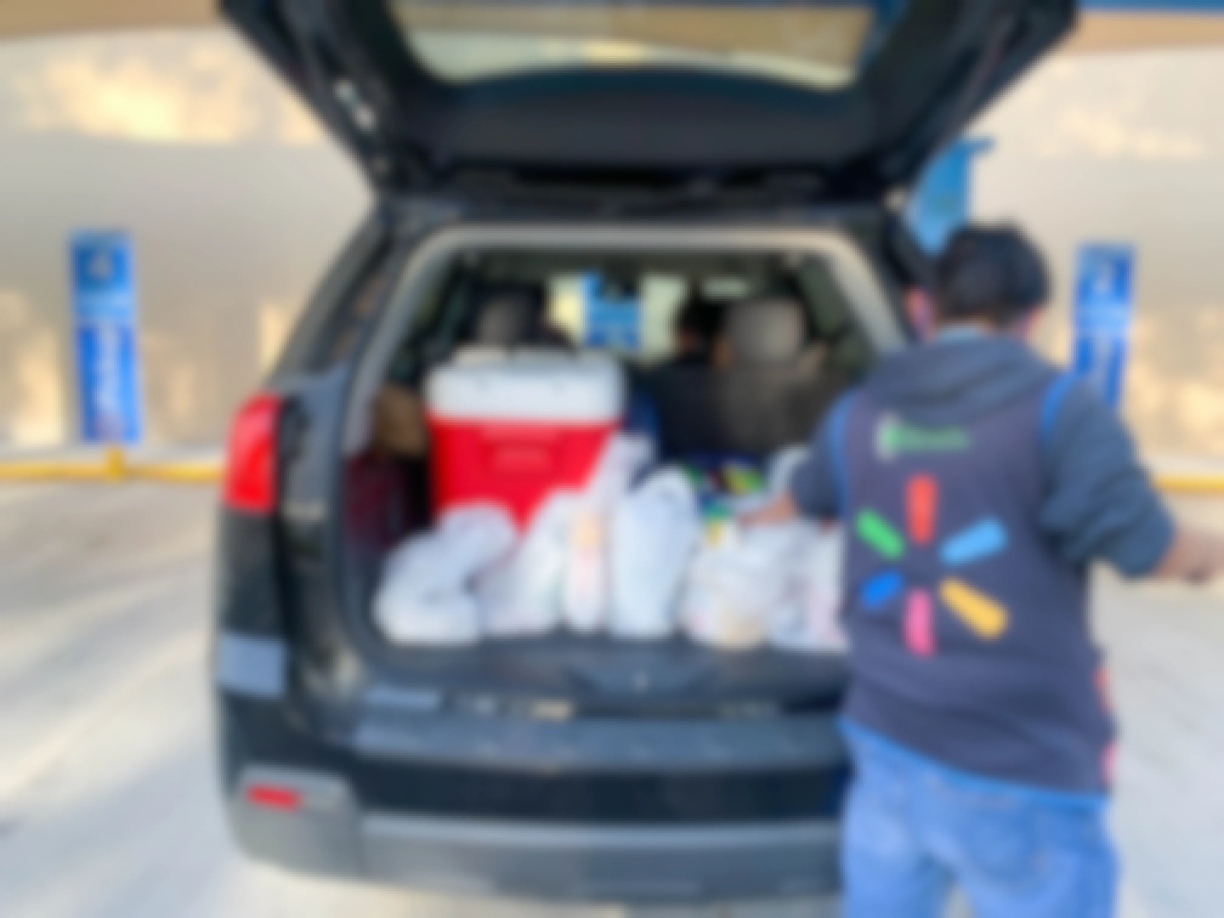 A Walmart employee loading groceries into the trunk of a vehicle parked in the Walmart Pickup spot.