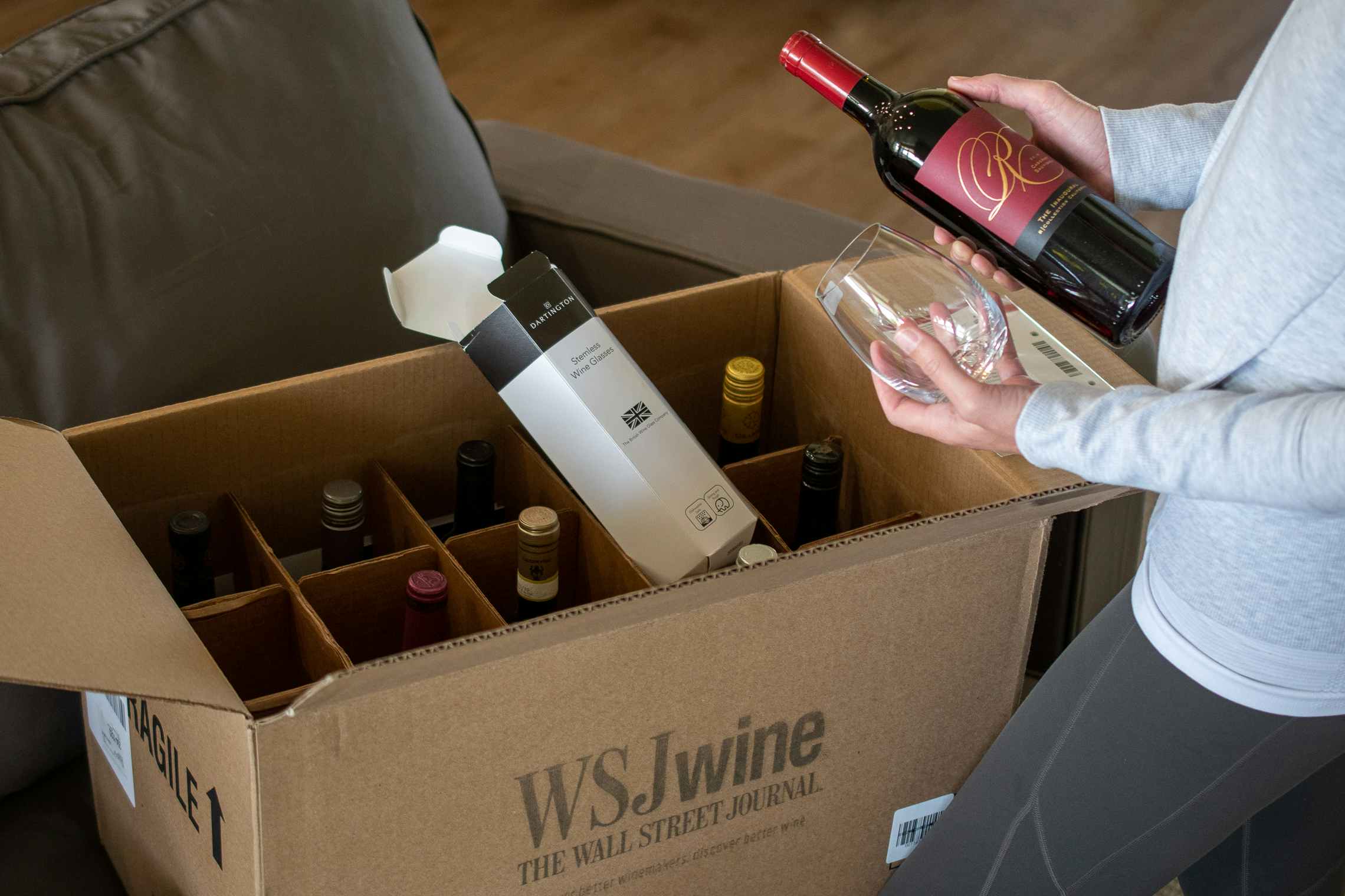 A woman holding a bottle of wine and stemless wine glass with a box filled with wine in front of her.