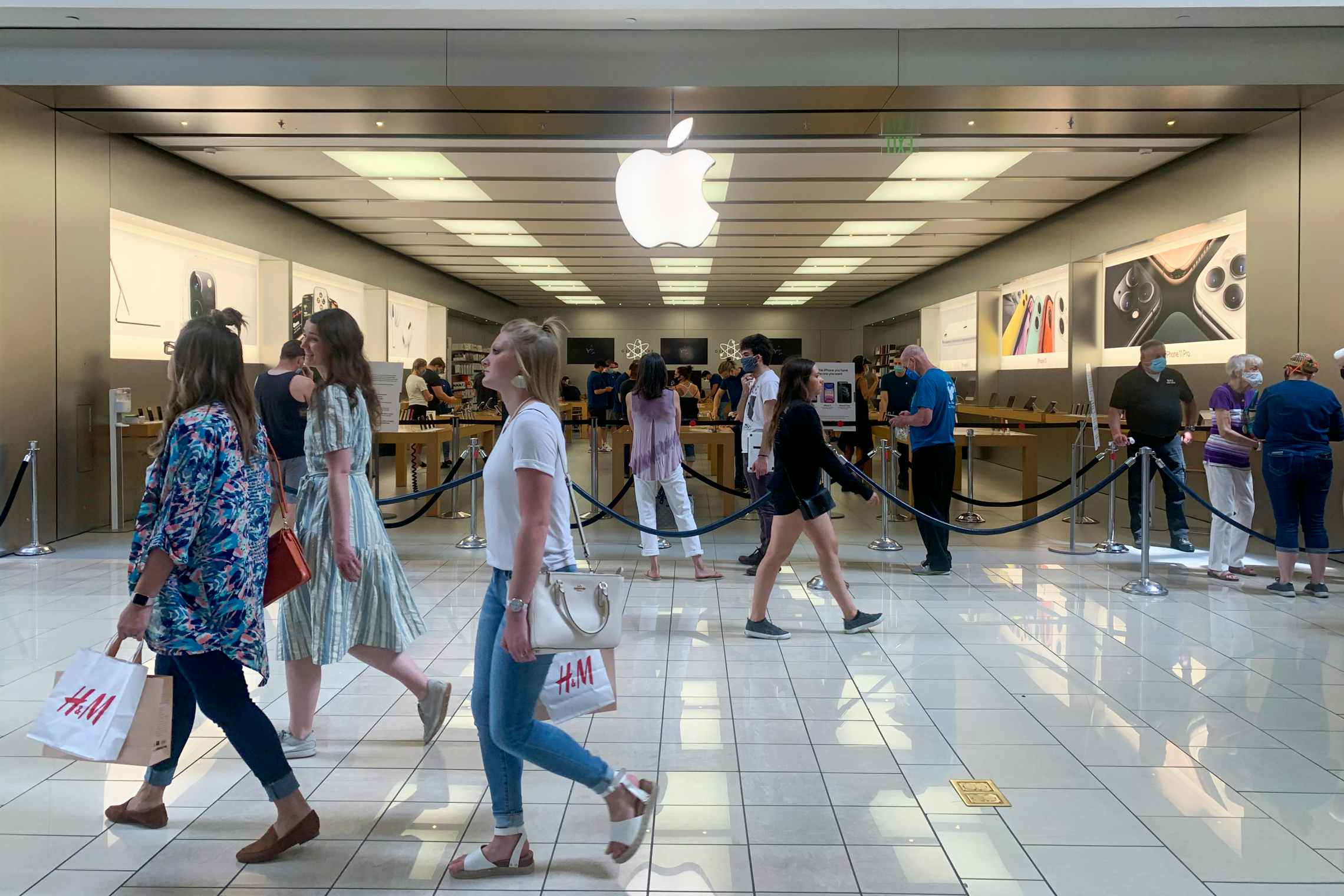 Customers wearing masks waiting in like to enter the Apple store inside a mall.