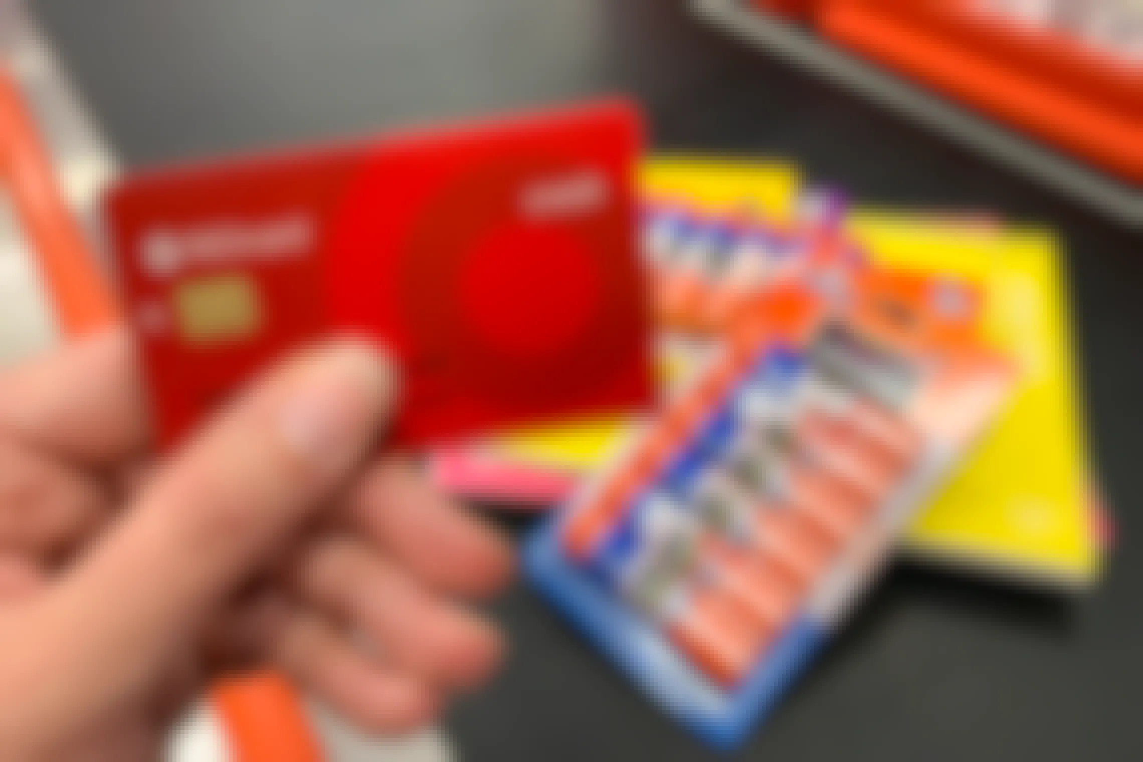 A person's hand holding their Target RedCard in front of a pile of school supplies on the conveyer belt at Target checkout. 