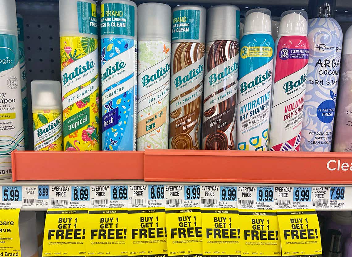 Bottles of Batiste dry shampoo on a shelf in a store with several BOGO sale tags.