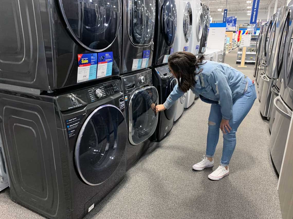 woman bends over and looks at a floor model washer at best buy