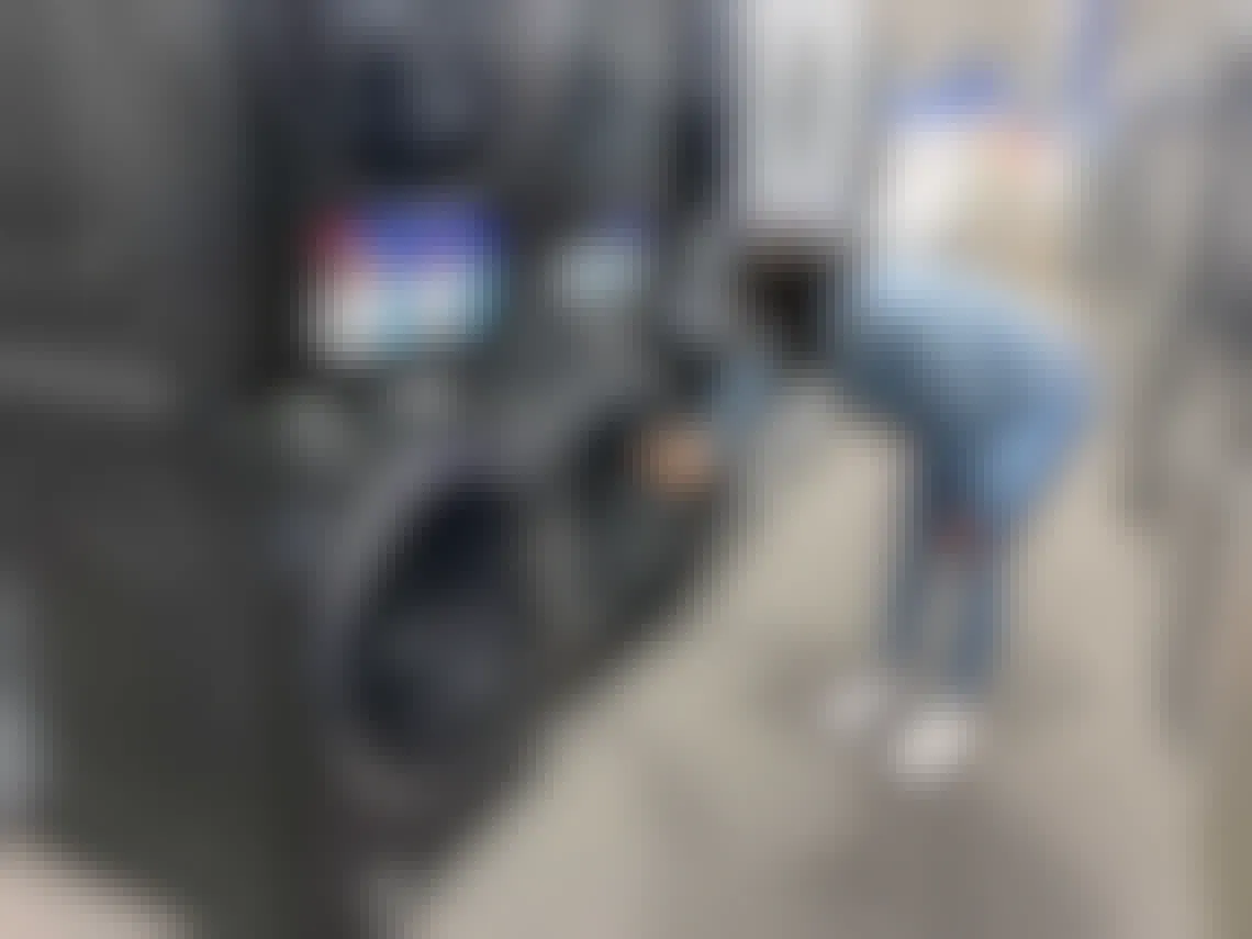 woman bends over and looks at a floor model washer at best buy
