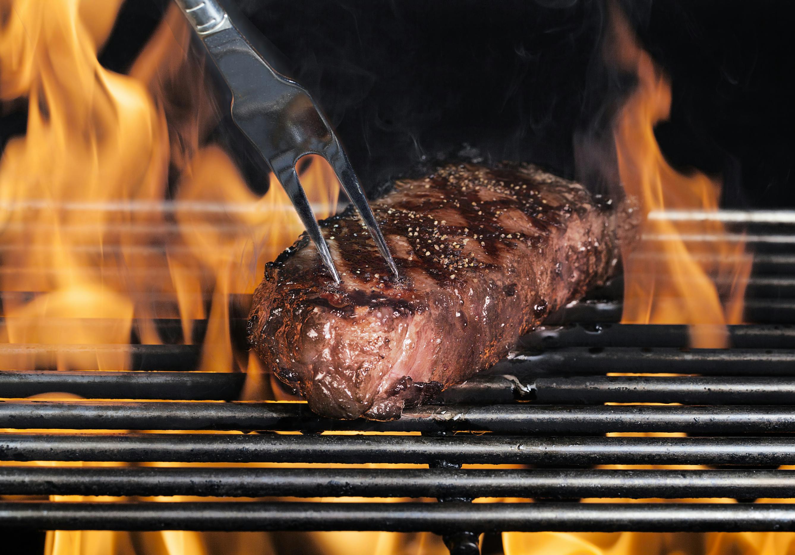 Steak on the grill, being poked with a fork as flame surround it.