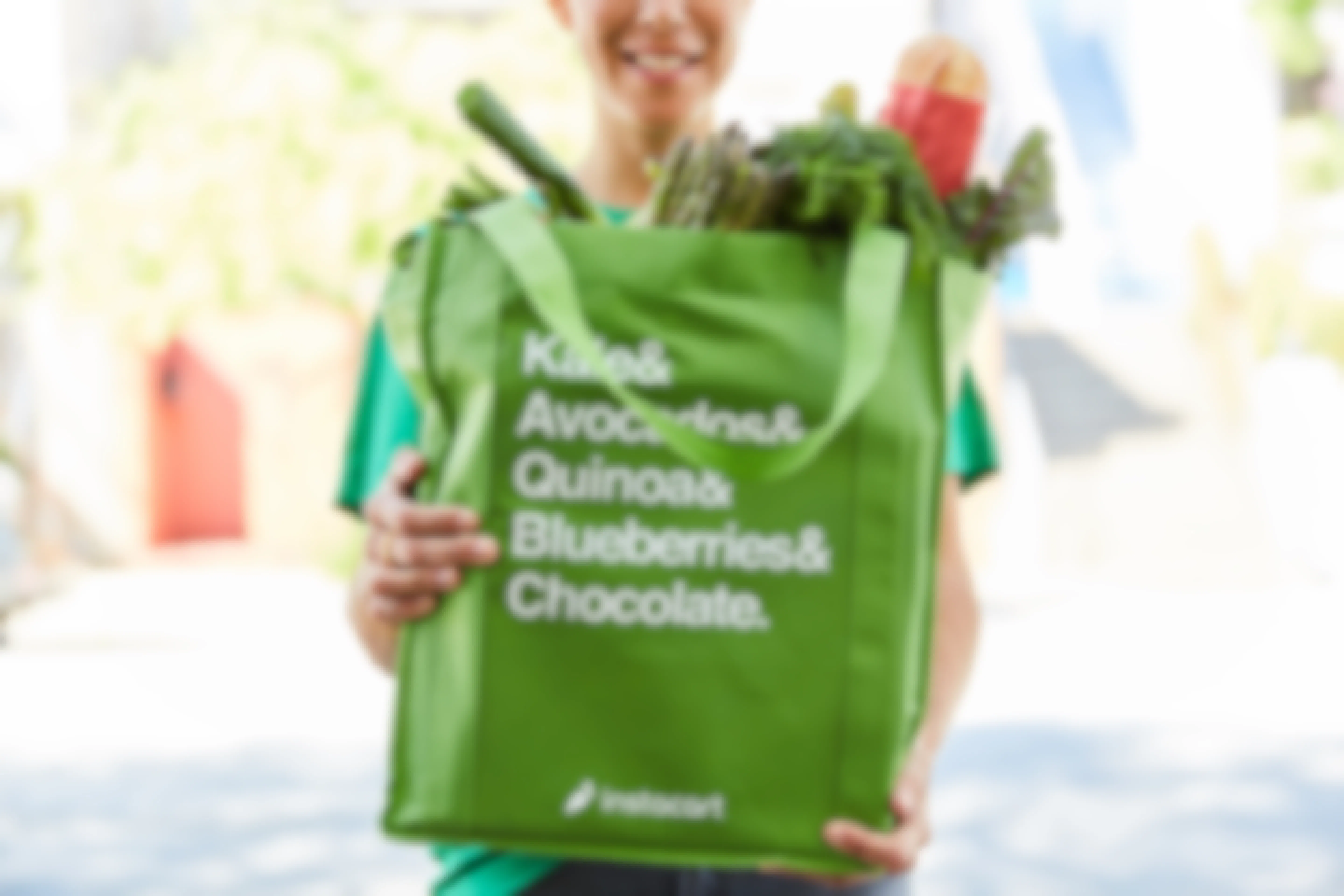 An Instacart delivery person holding Instacart shopping bag full of groceries.
