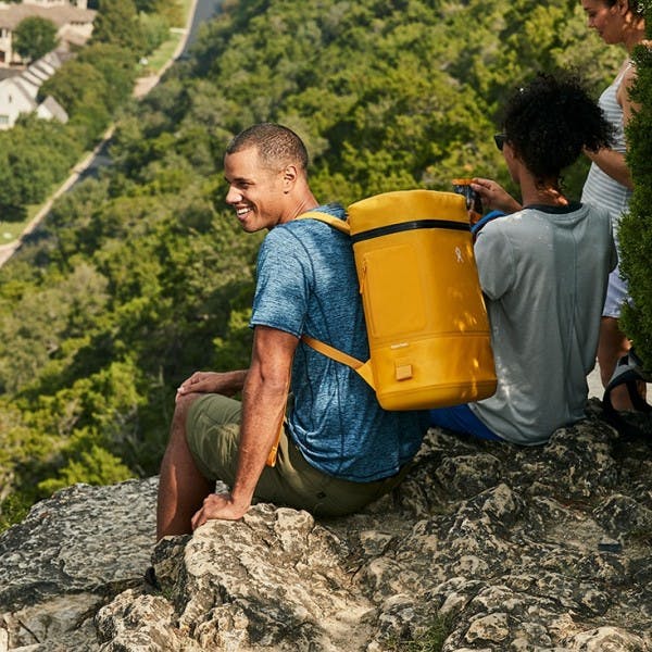 Man sits on rock outside with his hydroflask soft cooler on his back