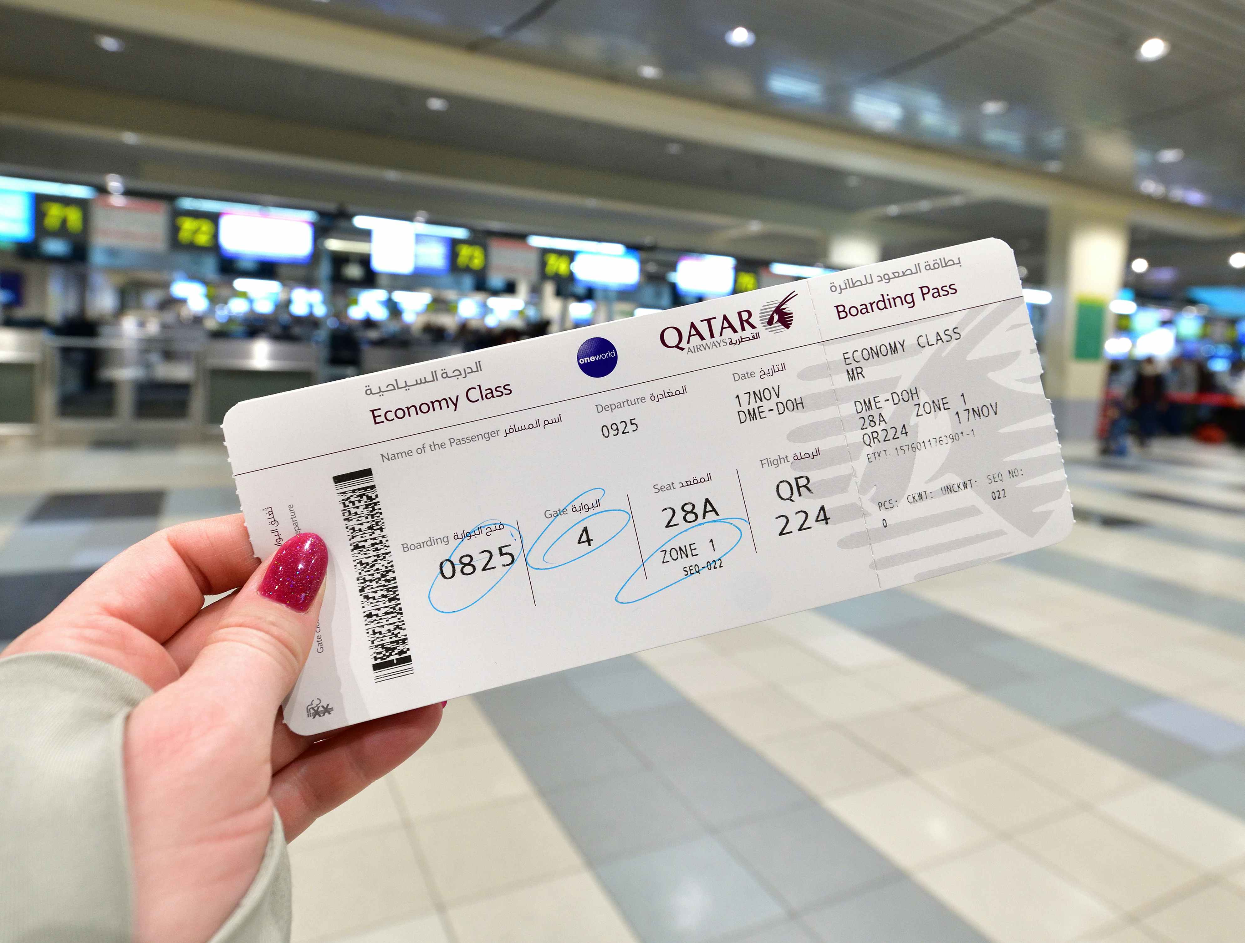 Woman in an airport holding a Qatar Airways boarding pass.