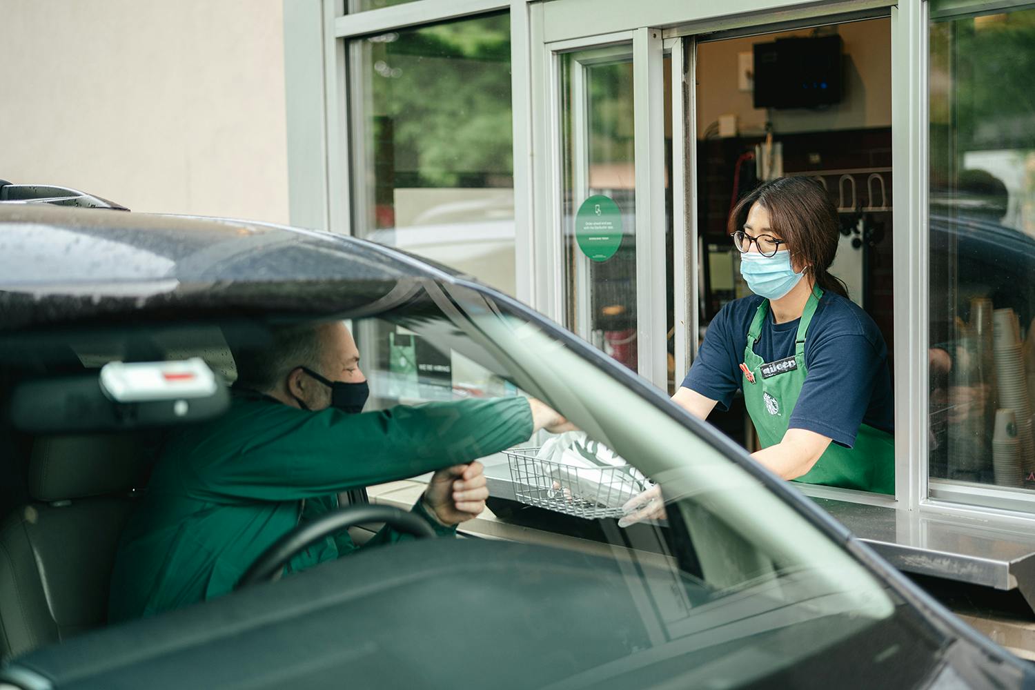 A Starbucks employee giving an order to a customer in their vehicle through the drive-thru window.