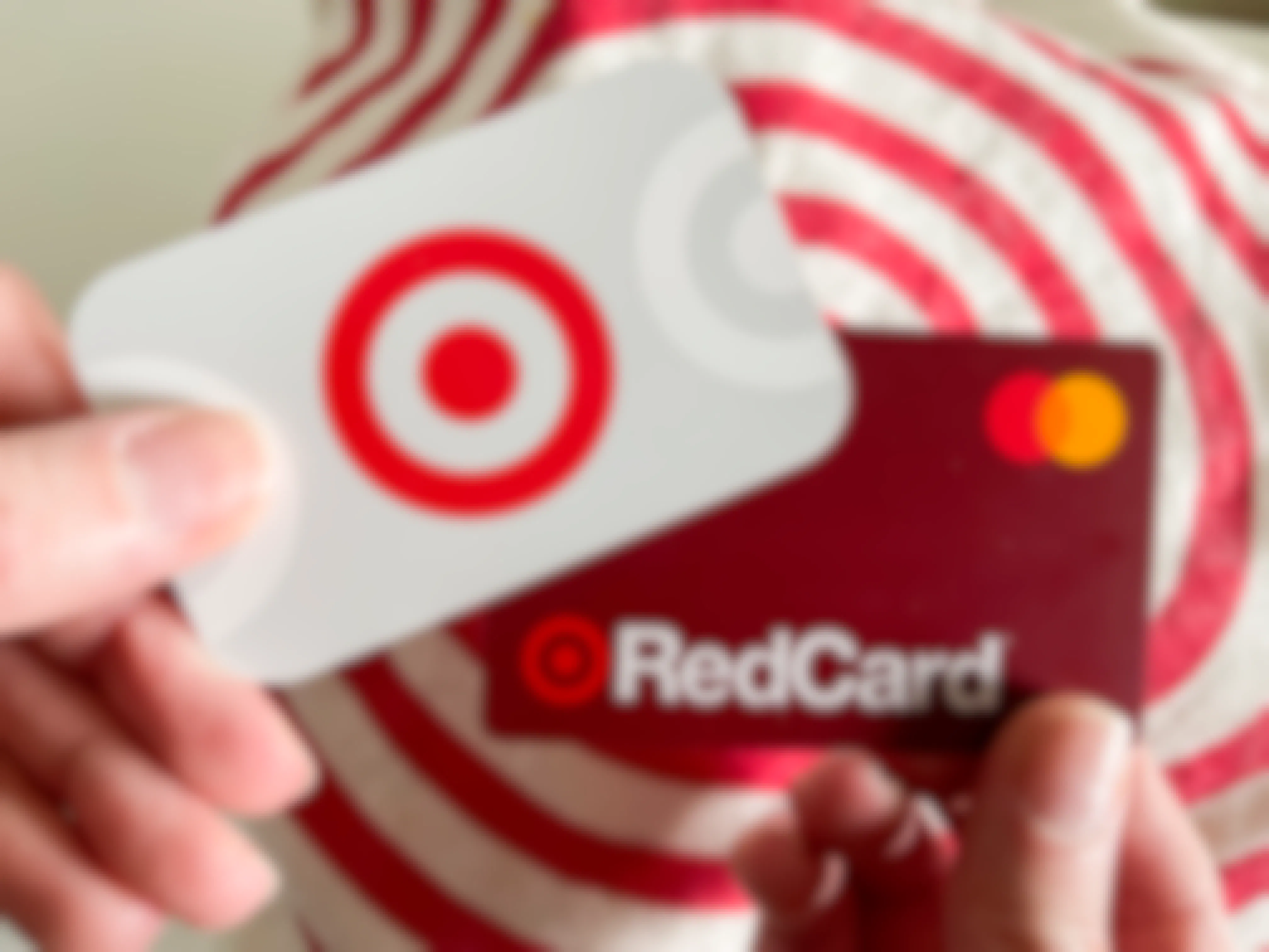 A person's hands, one holding a Target gift card, and the other holding a Target RedCard, in front of a Target bag.