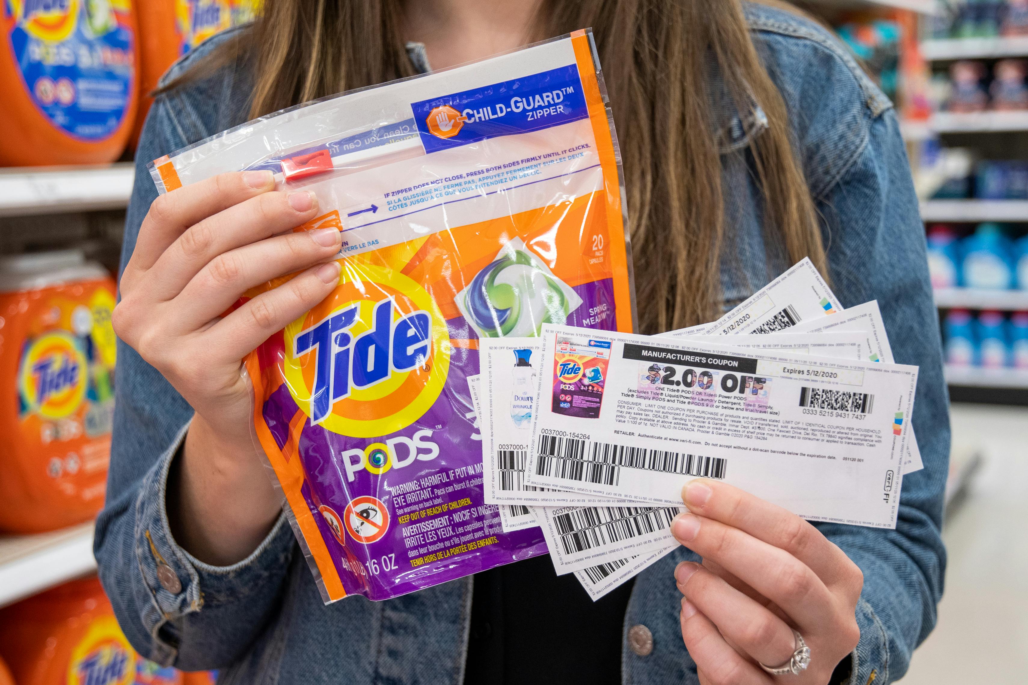 A woman holding a pack of tide Pods with printed manufacture coupons in hand.