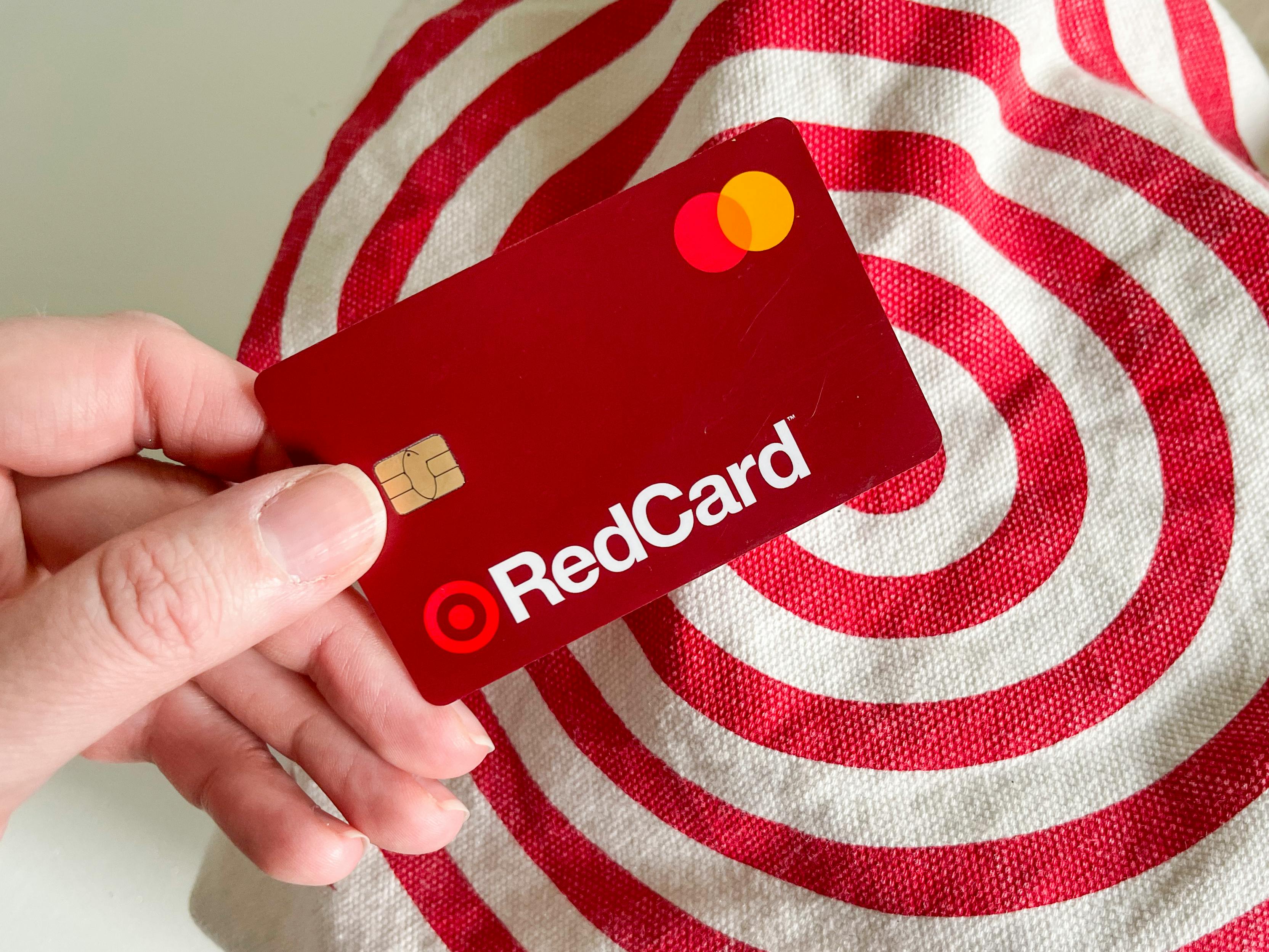 A person's hand holding a Target RedCard above a reusable Target shopping bag.
