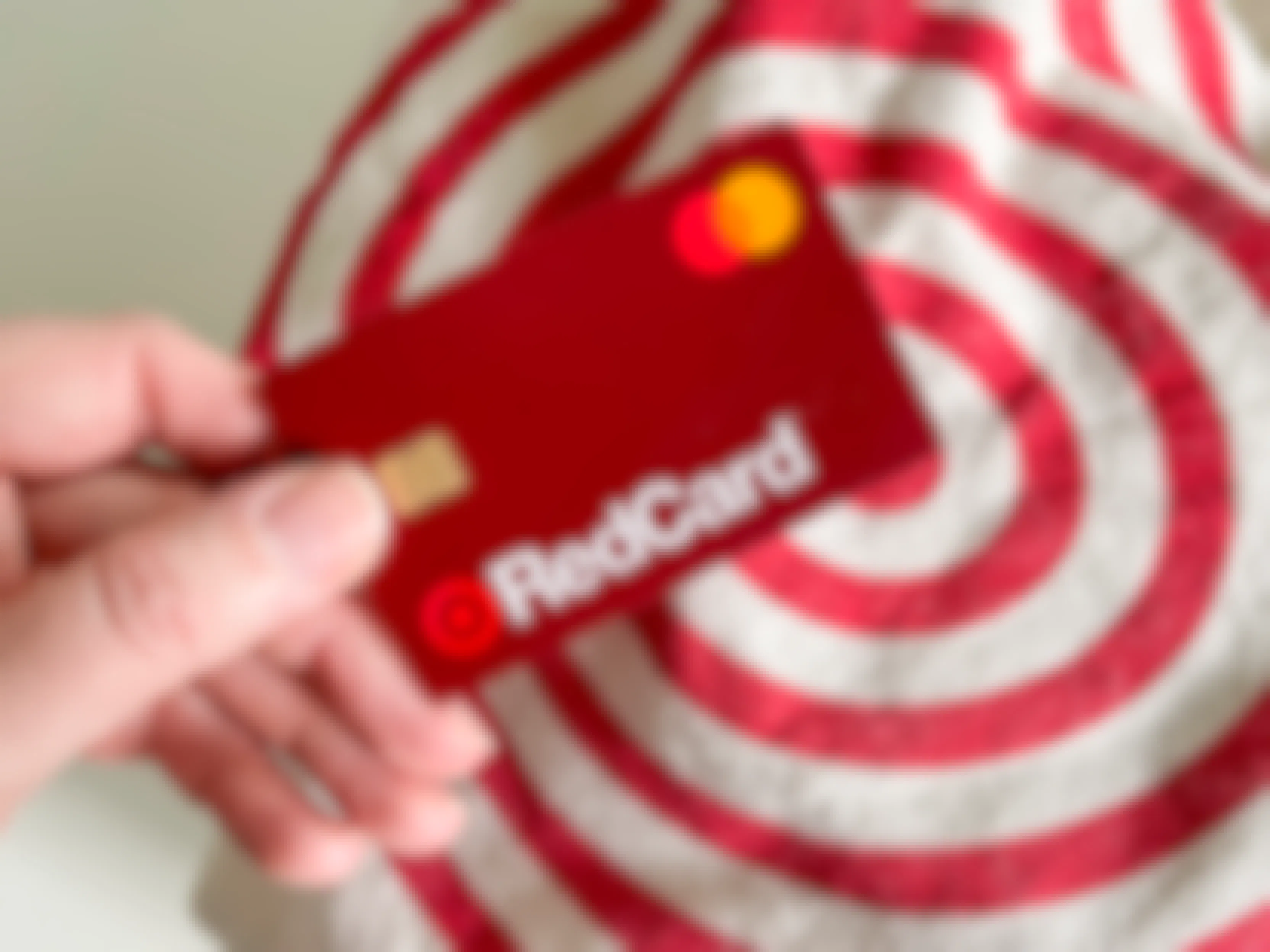 A person's hand holding a Target RedCard above a reusable Target shopping bag.