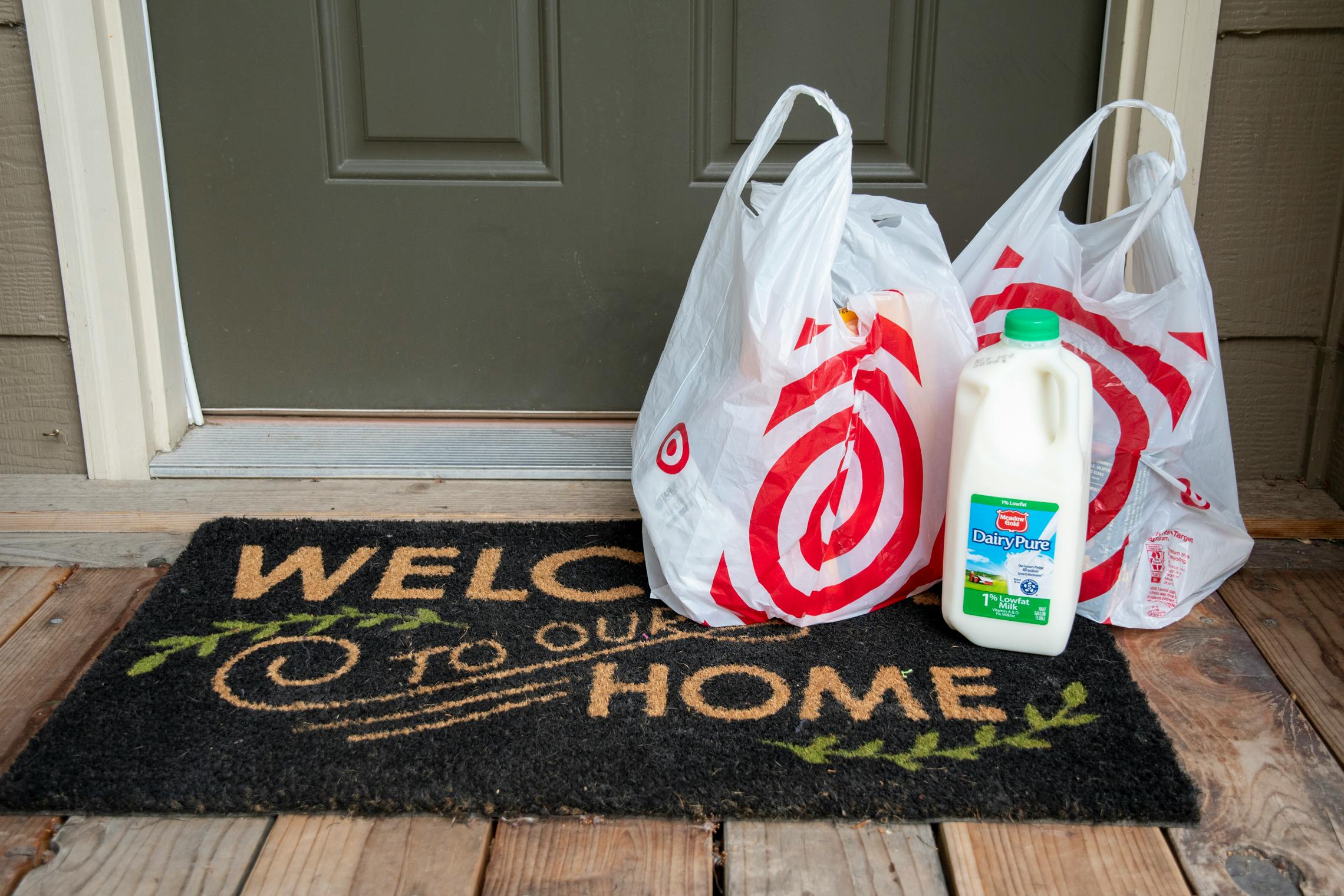 A Target Shipt grocery delivery order sitting on a front porch doormat that reads, "Welcome to our Home