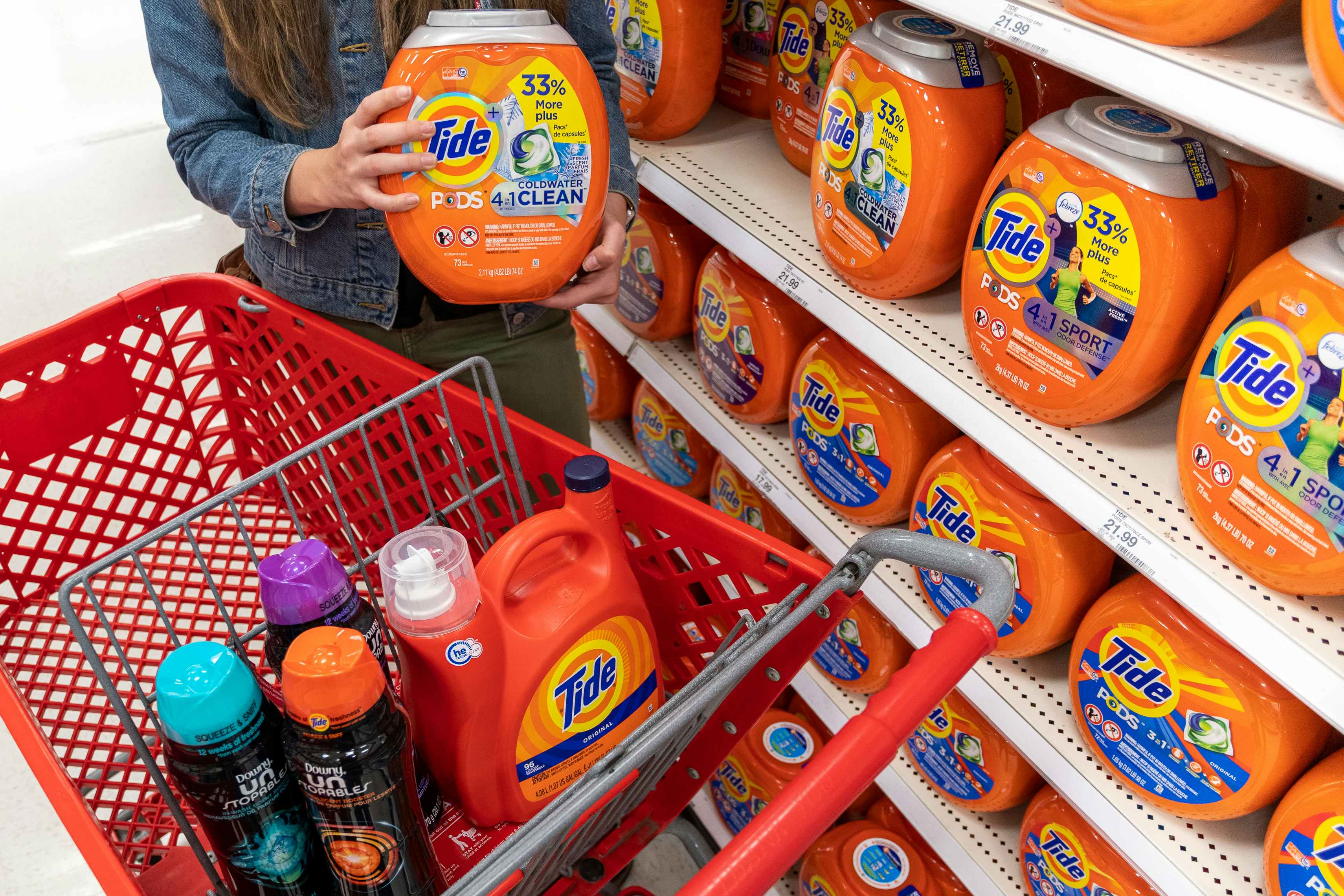 A woman standing behind a red Target shopping cart, holding a container of tide pods, with other laundry products in the shopping cart.
