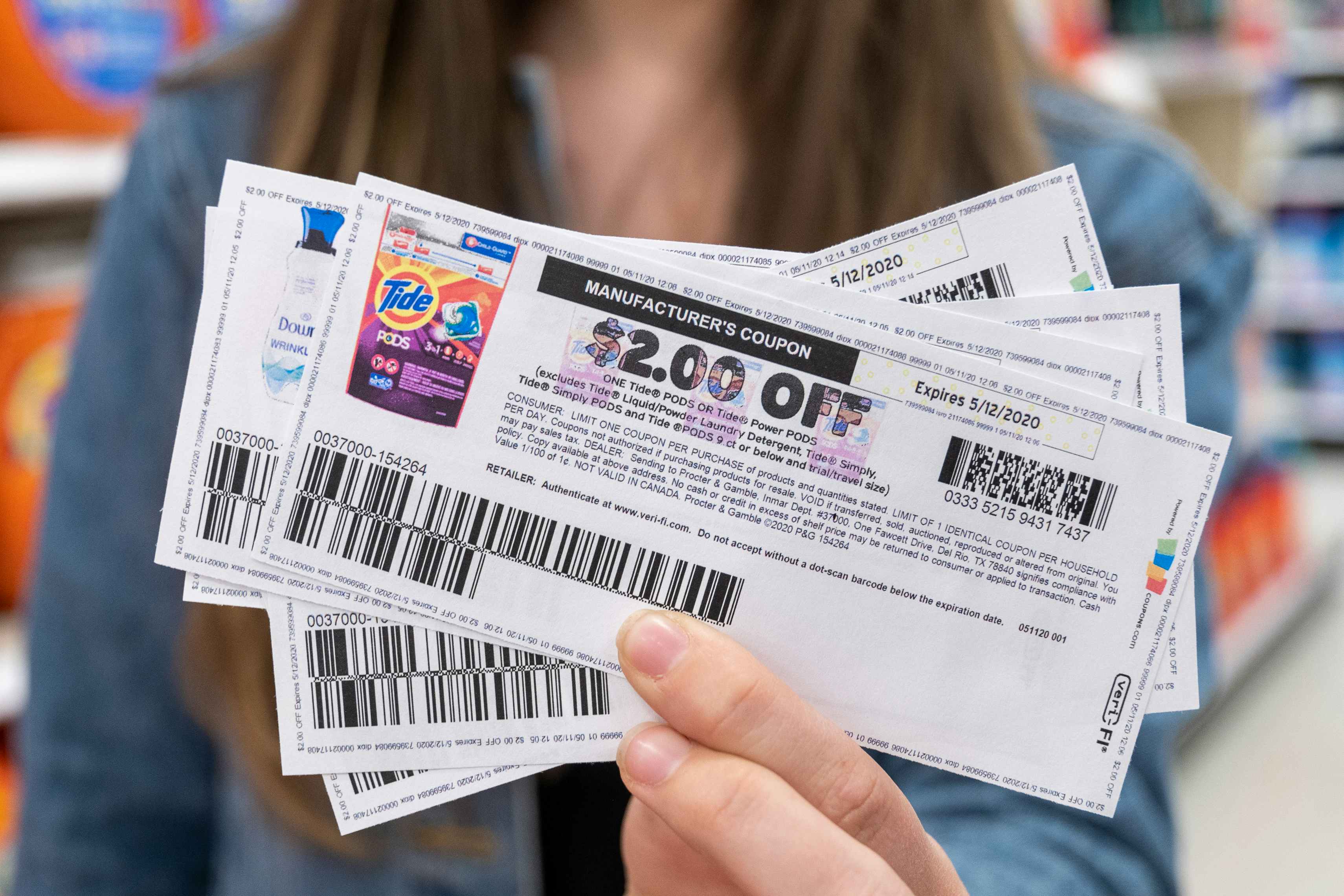 A woman holding out a stack of manufacture coupons. The coupon on top is for $2 off Tide Pods.
