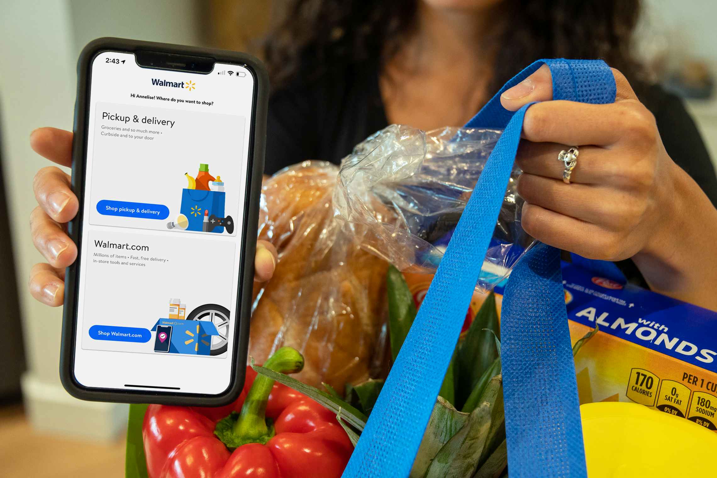 Woman holding a bag of Walmart groceries in one hand with a cell phone with the Walmart app on the other.