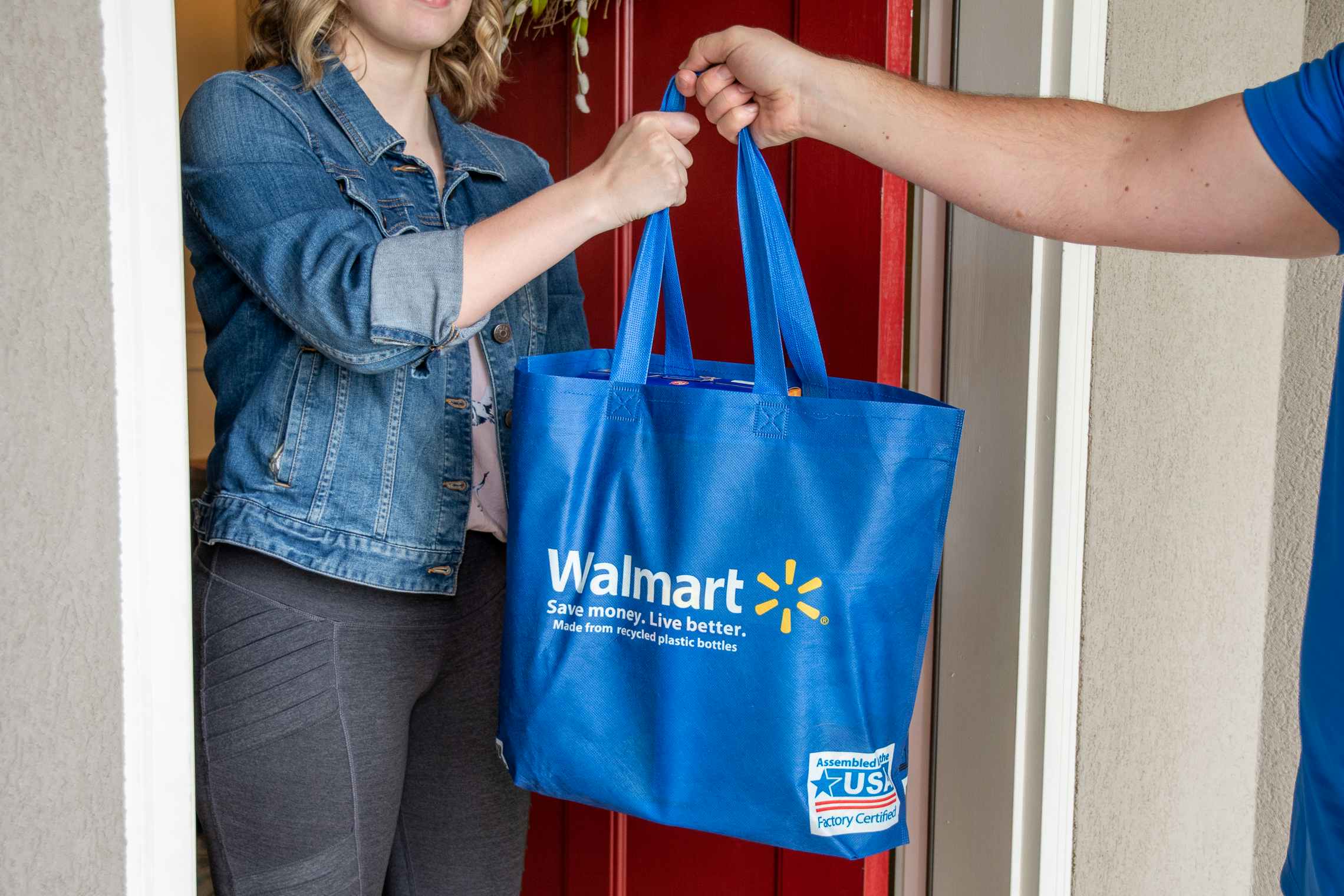 A delivery person handing a Walmart bag to a woman in her front doorway.