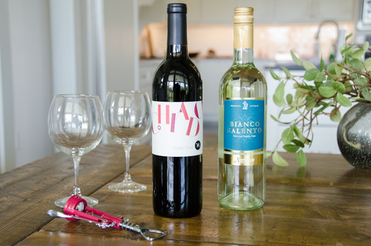 Two bottles of wine, a bottle opener, and two wine glasses sitting on a table.