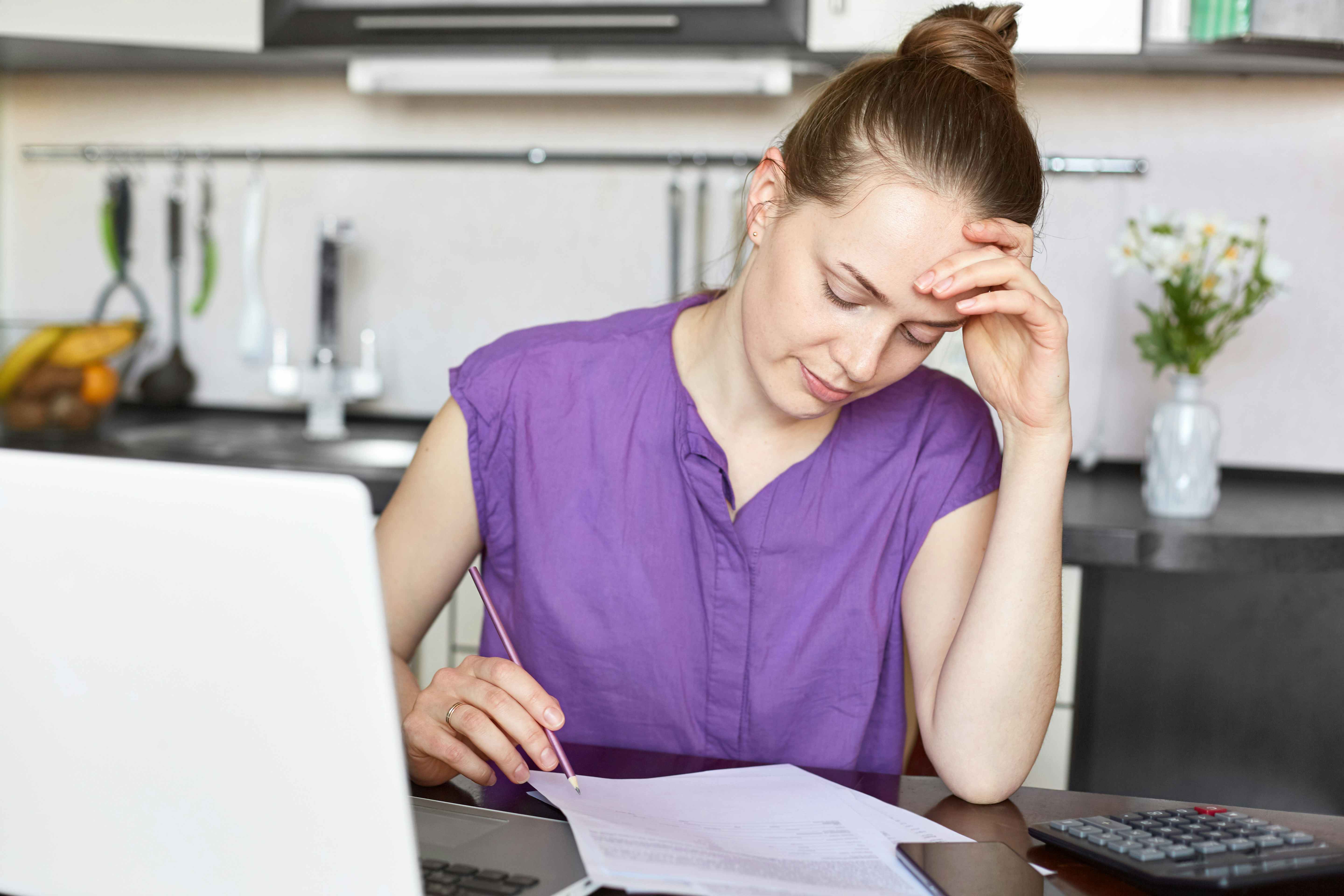 Worried looking woman looking at paperwork or bills in front of a computer and calculator