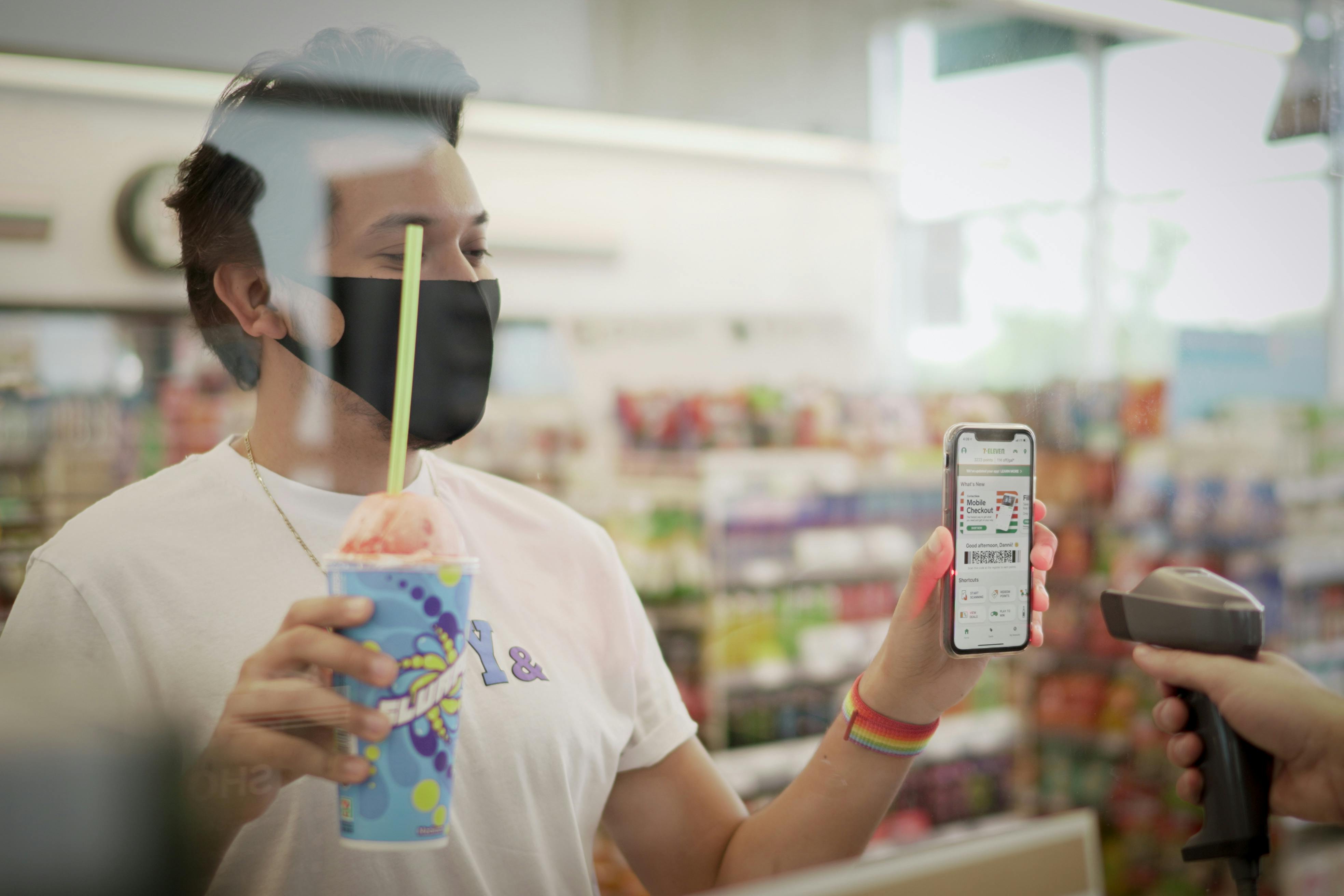 A person holding a slurpee and their phone displaying a coupon for a free slurpee to be scanned by a 7/11 employee at checkout.