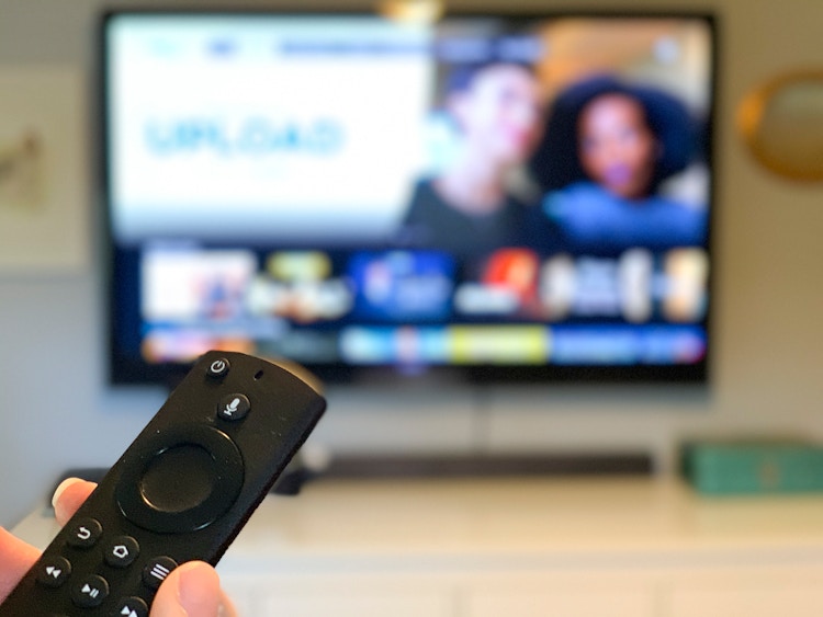 Amazon fire tv stick pointed at a tv with programs out of focus in the background.