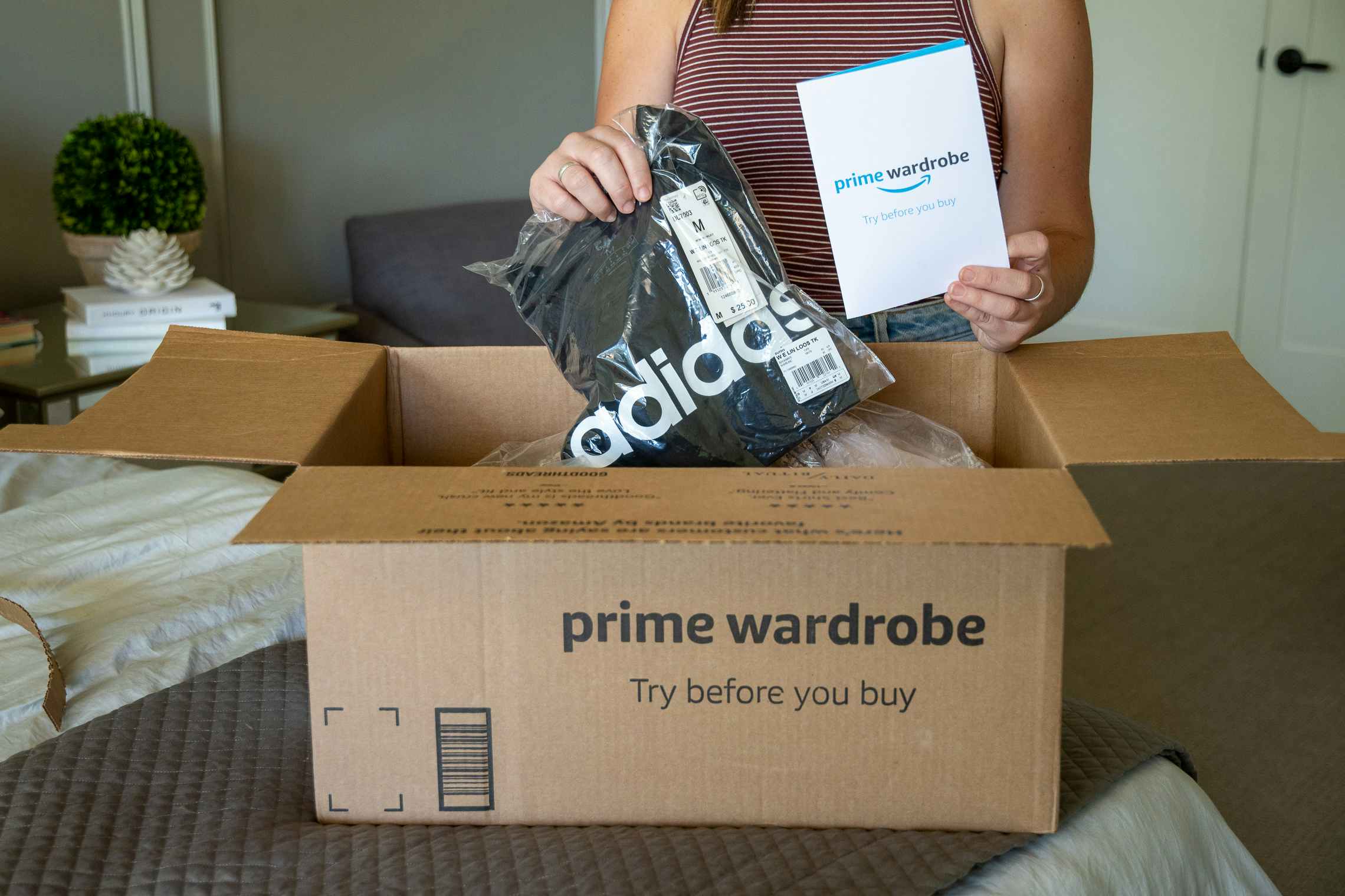 A woman pulling an adidas tank top and amazon wardrobe pamphlet from a box.