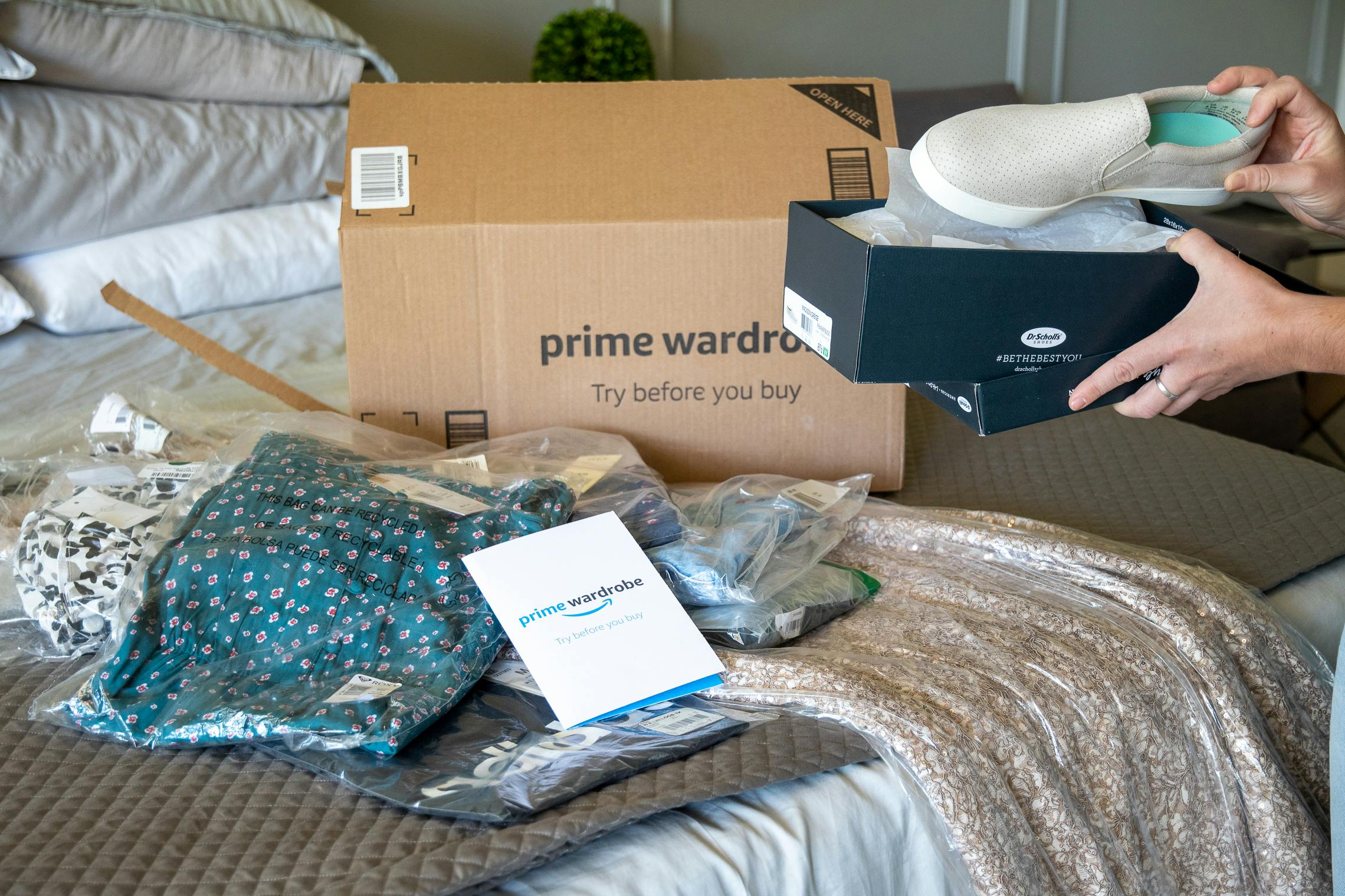 A woman looking at a pair of shoes ordered from Amazon Prime wardrobe with items from an order box in the background. 