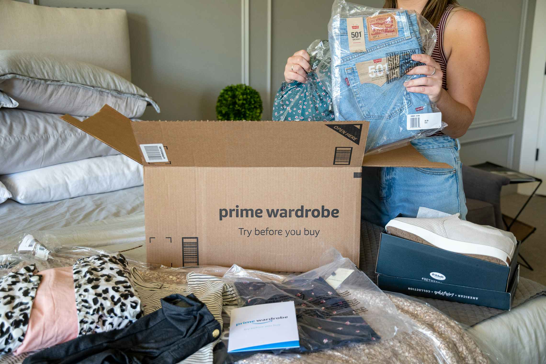 A woman unpacking an Amazon prime wardrobe order from a box on her bed.