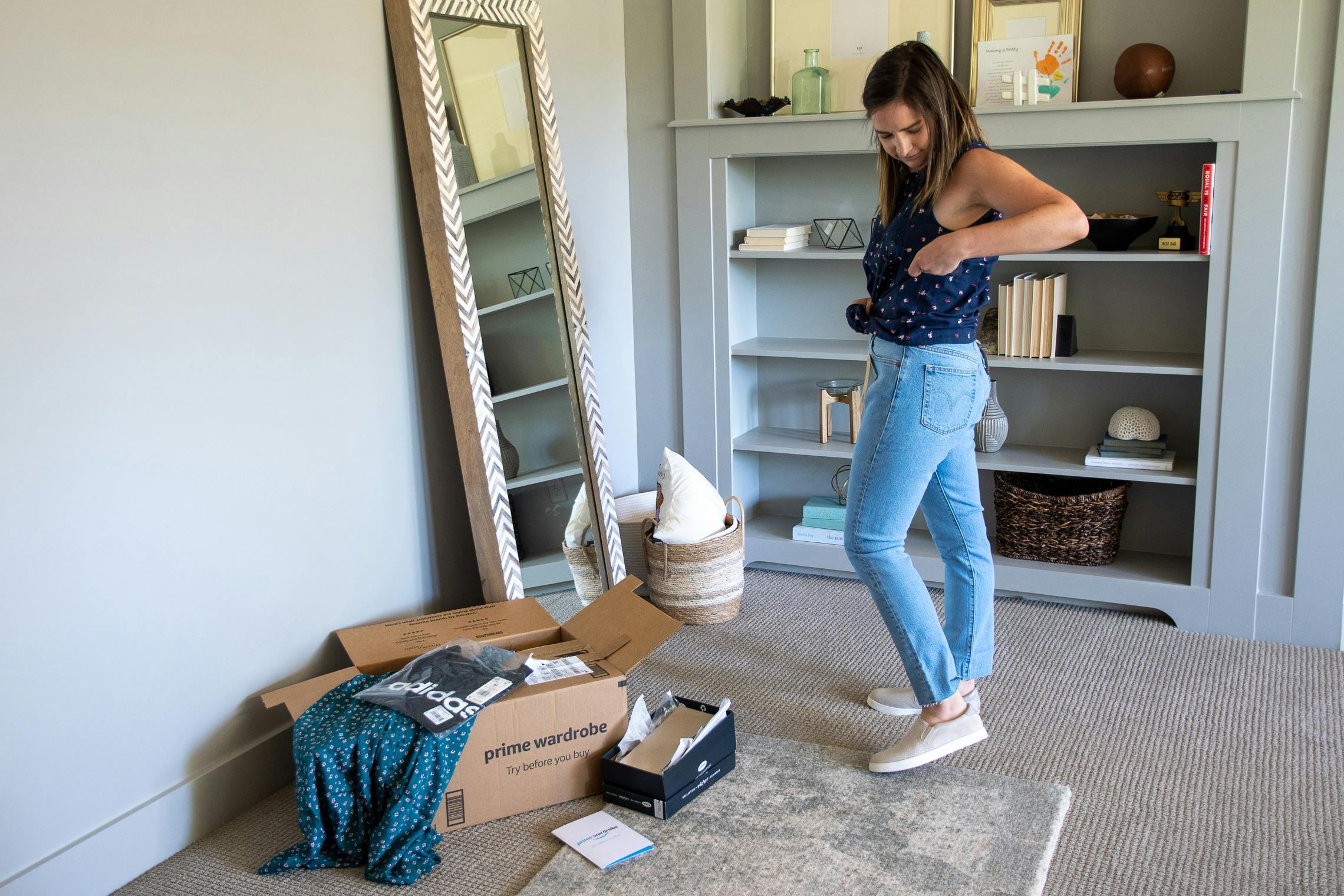 A woman trying on clothes in her home with an amazon prime wardrobe box near by