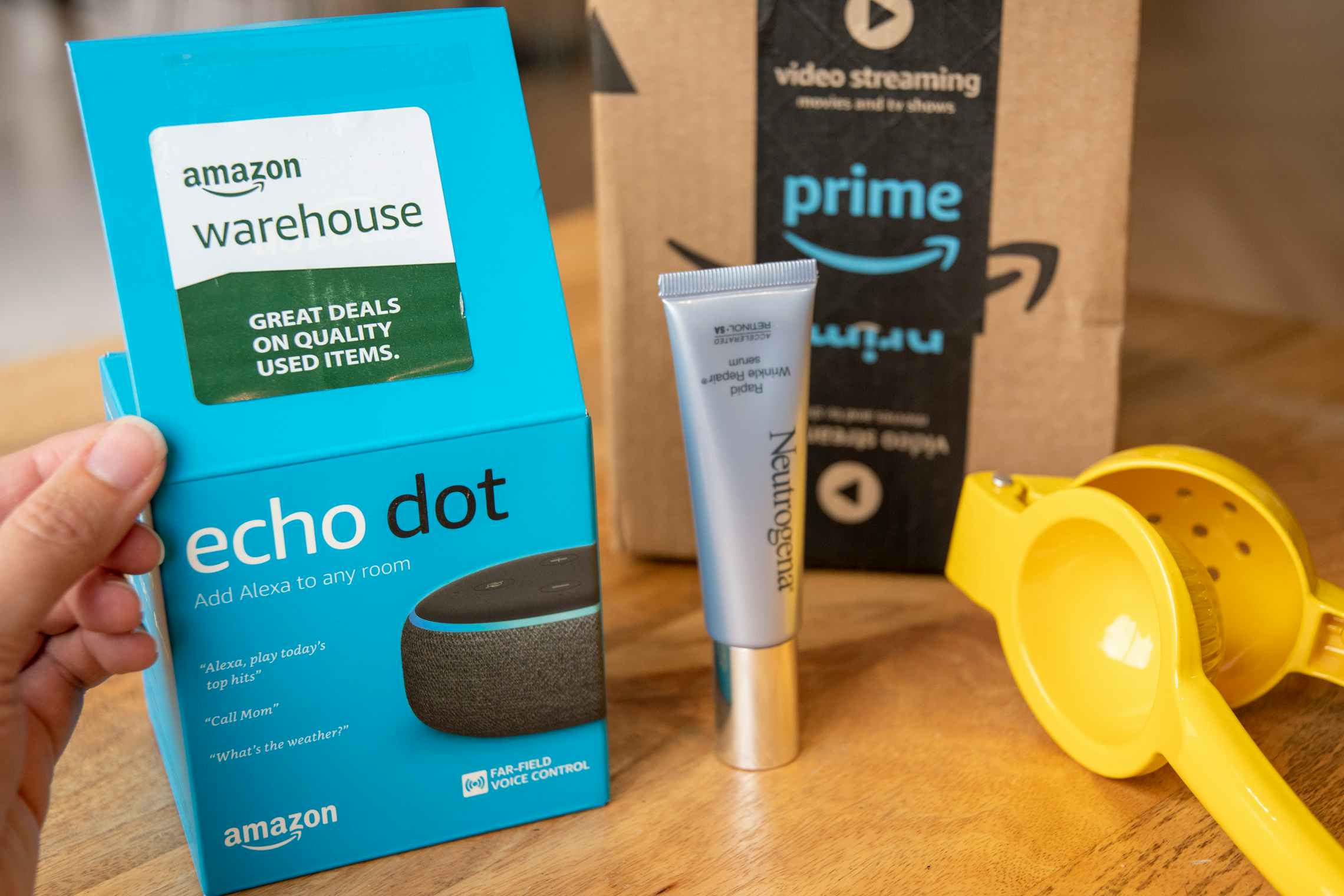 A person showing the Amazon Warehouse sticker on the lid of an Amazon Echo box on a table next to more products and a prime shipping box.