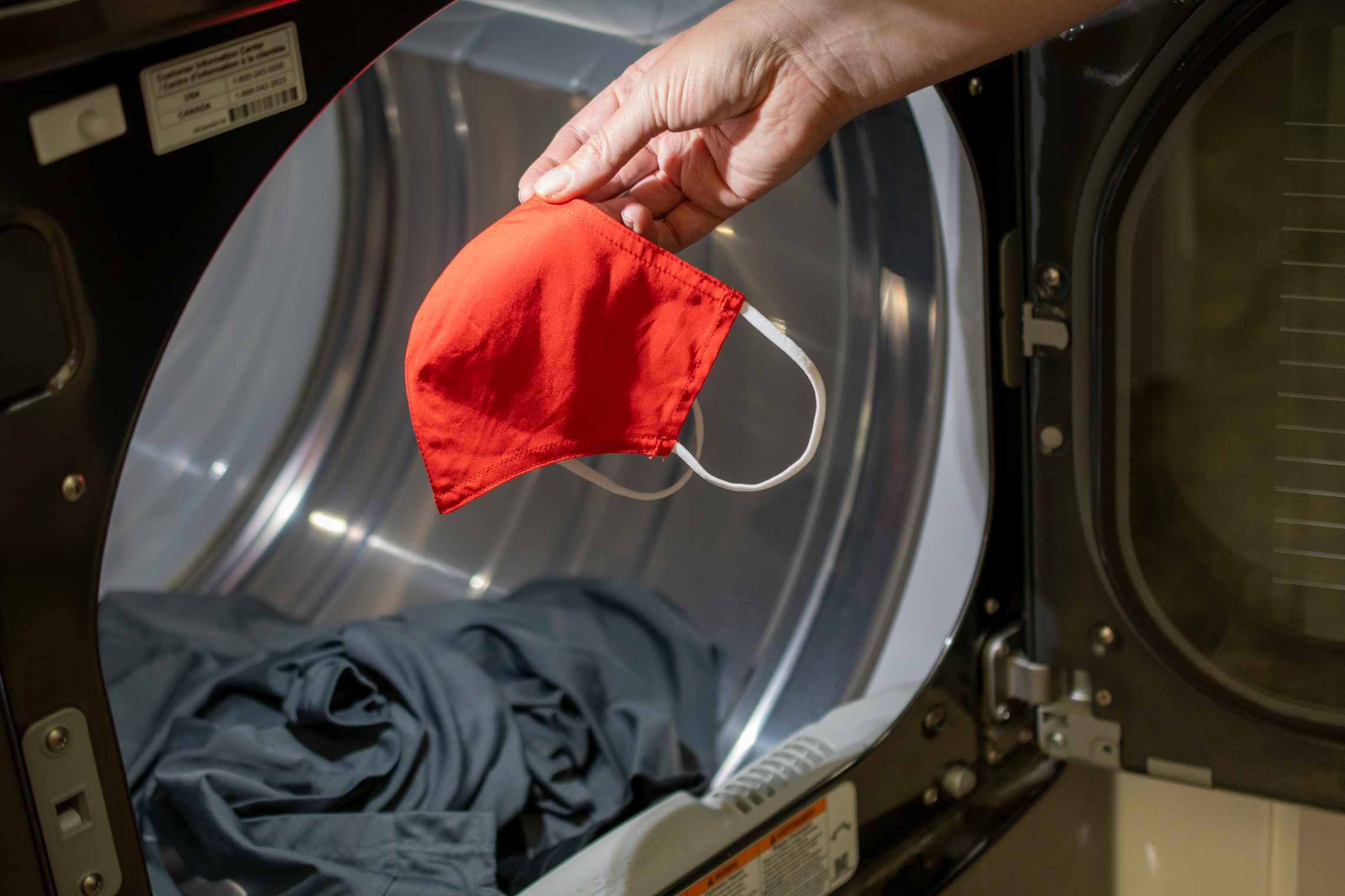A hand tossing a fabric face mask into a dryer.