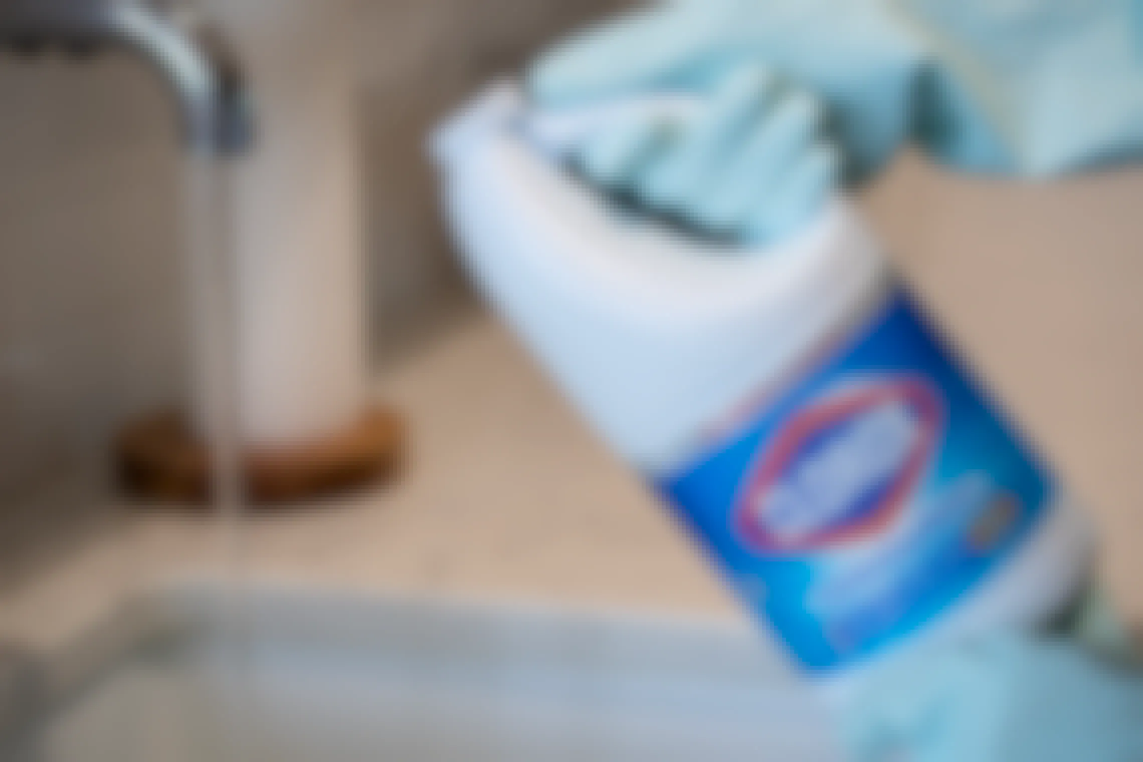 A person holding a bottle of Clorox bleach next to a sink with the tap running while wearing rubber dish gloves.