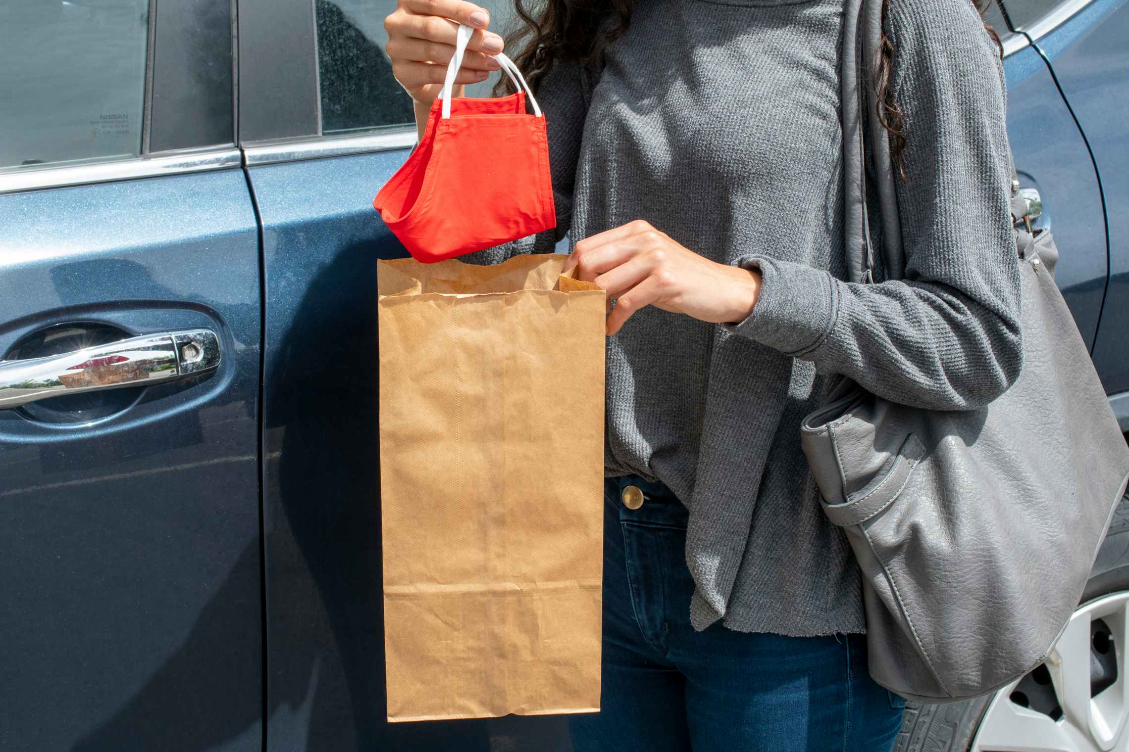 A woman putting a fabric face mask into a brown paper bag.