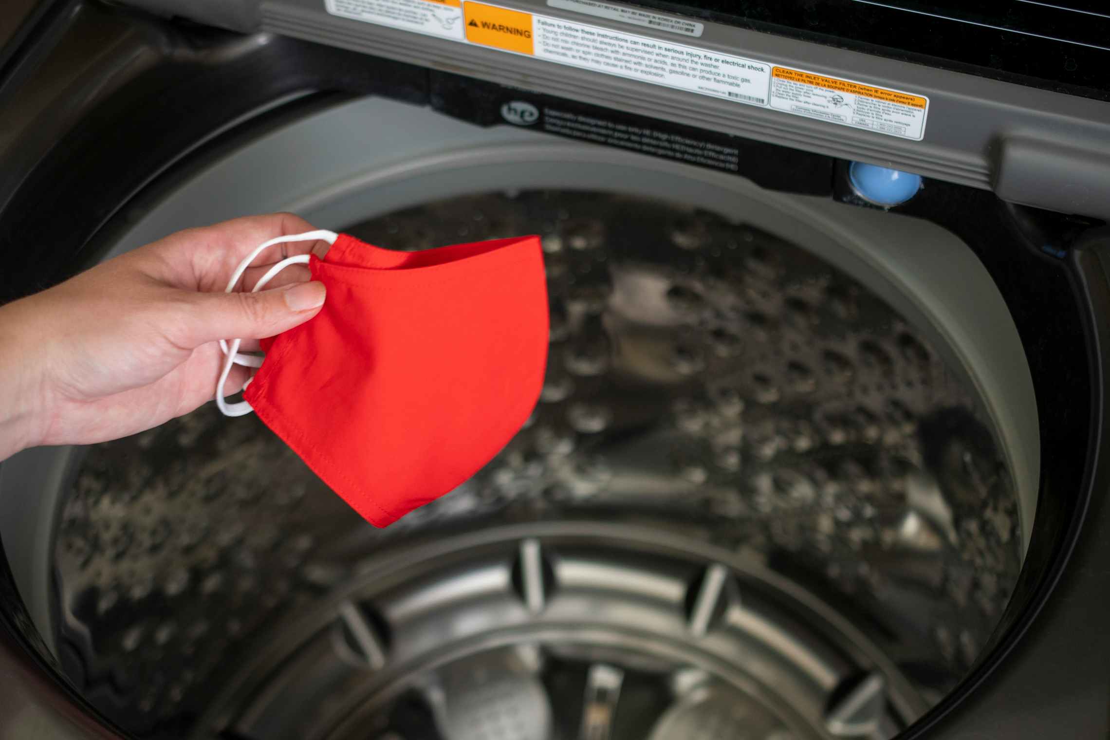 A hand tossing a fabric face mask into a washing machine.