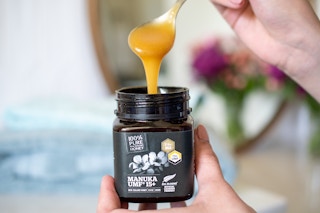 A spoon dripping Manuka honey over the jar.