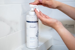 A woman pumping soap from a bottle of Ivory body wash in a shower.
