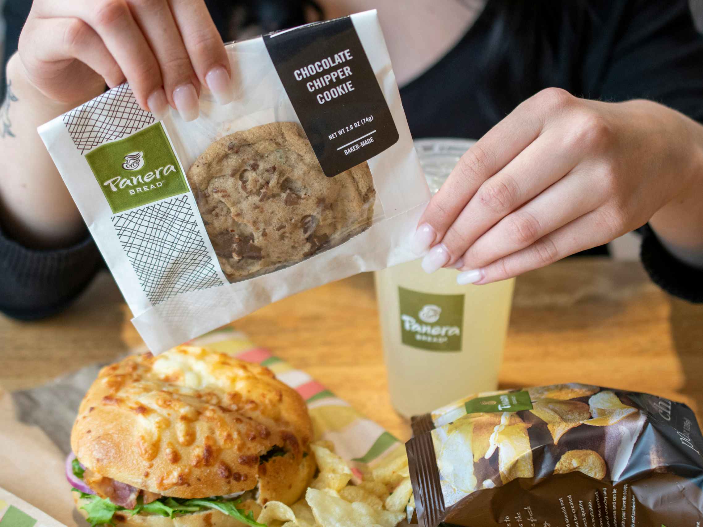 A person holding a Chocolate Chipper cookie next to a Panera meal.