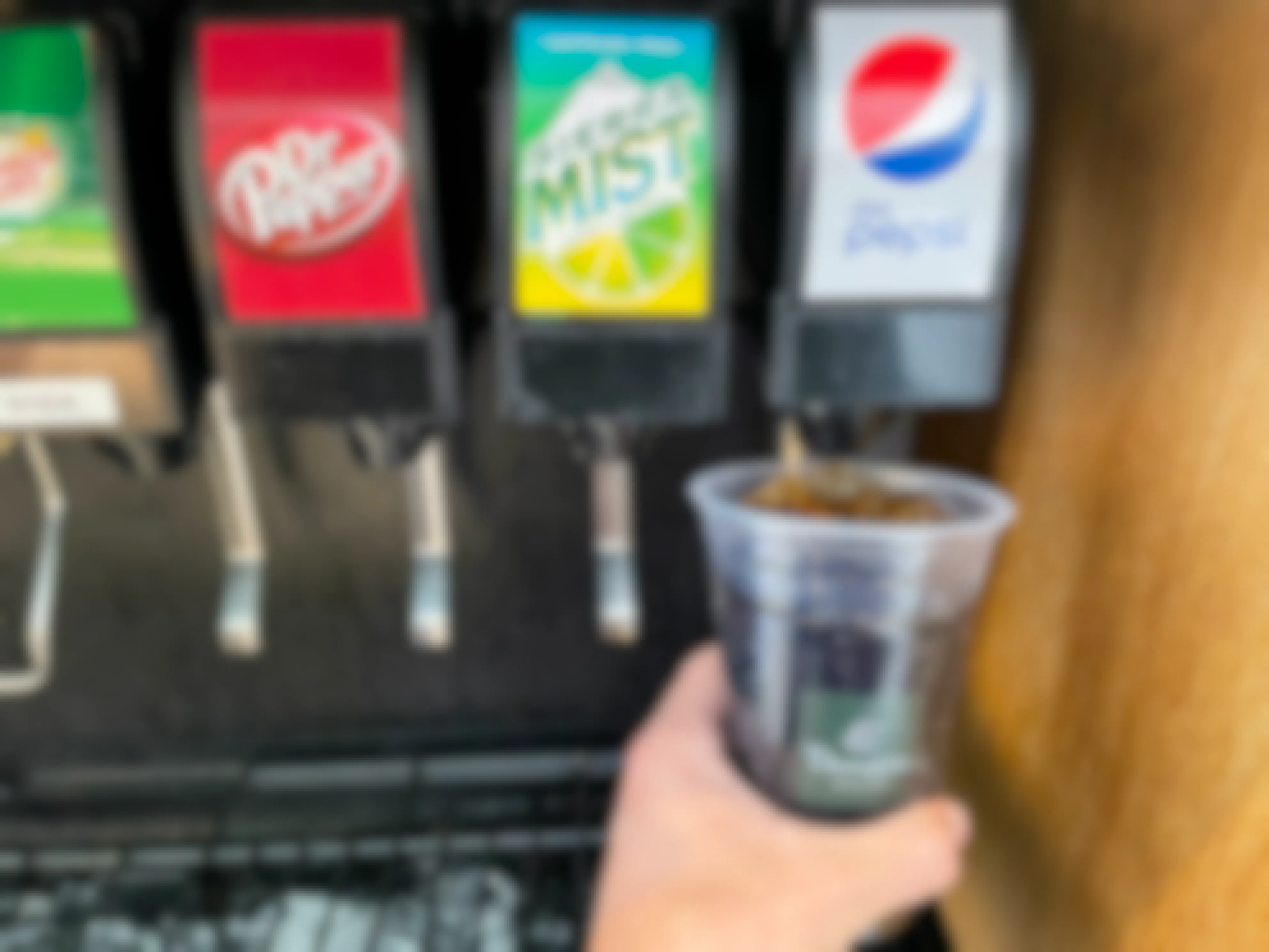 A person's hand filling a Panera drink cup with Diet Pepsi at the fountain drink machine.