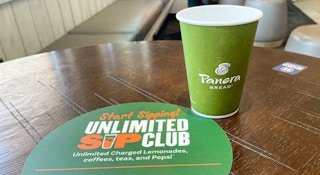 A panera bread cup next to an unlimited sip club sticker on a table.