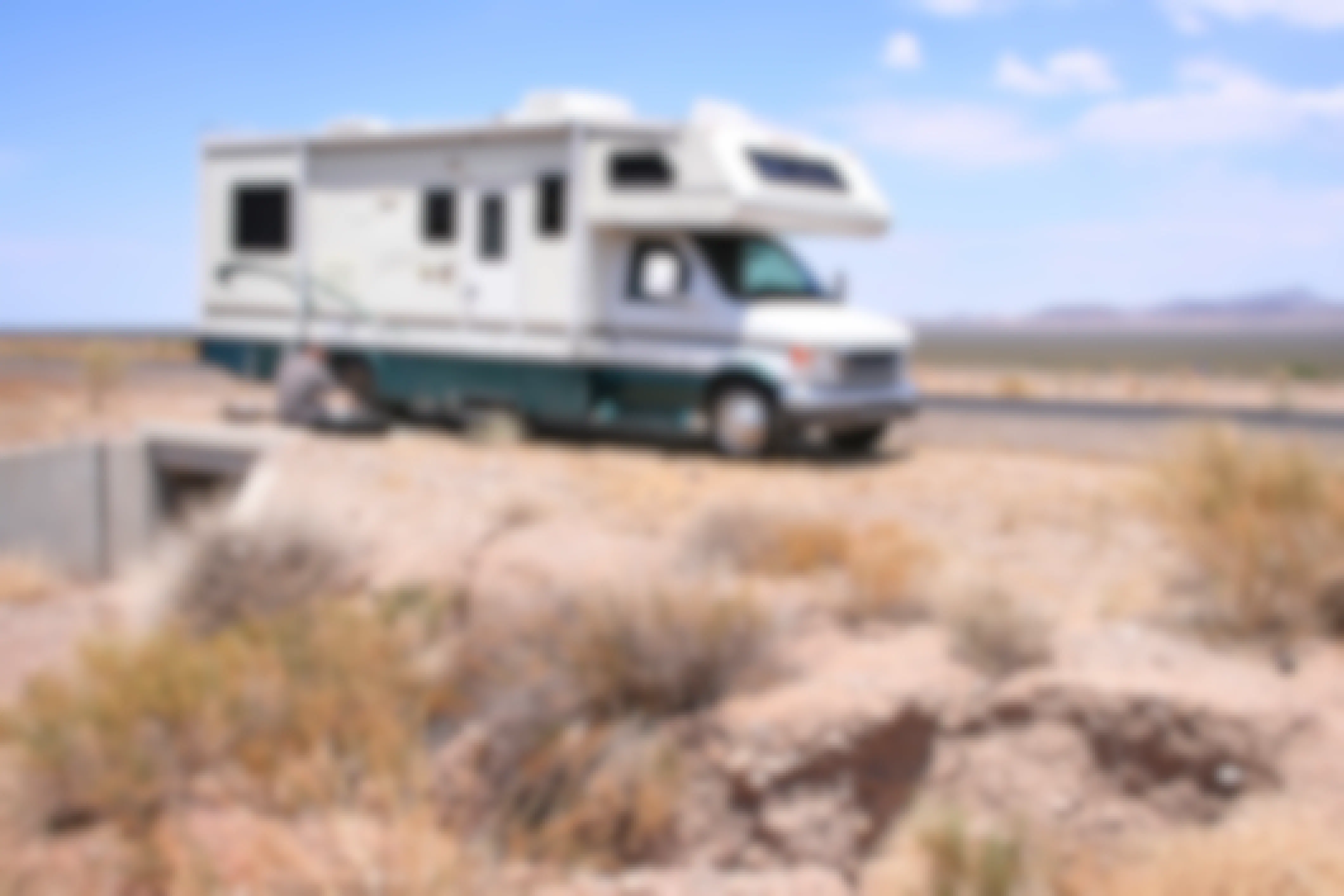 RV Motorhome on the side of a desert road, with the driver fixing a flat tire.